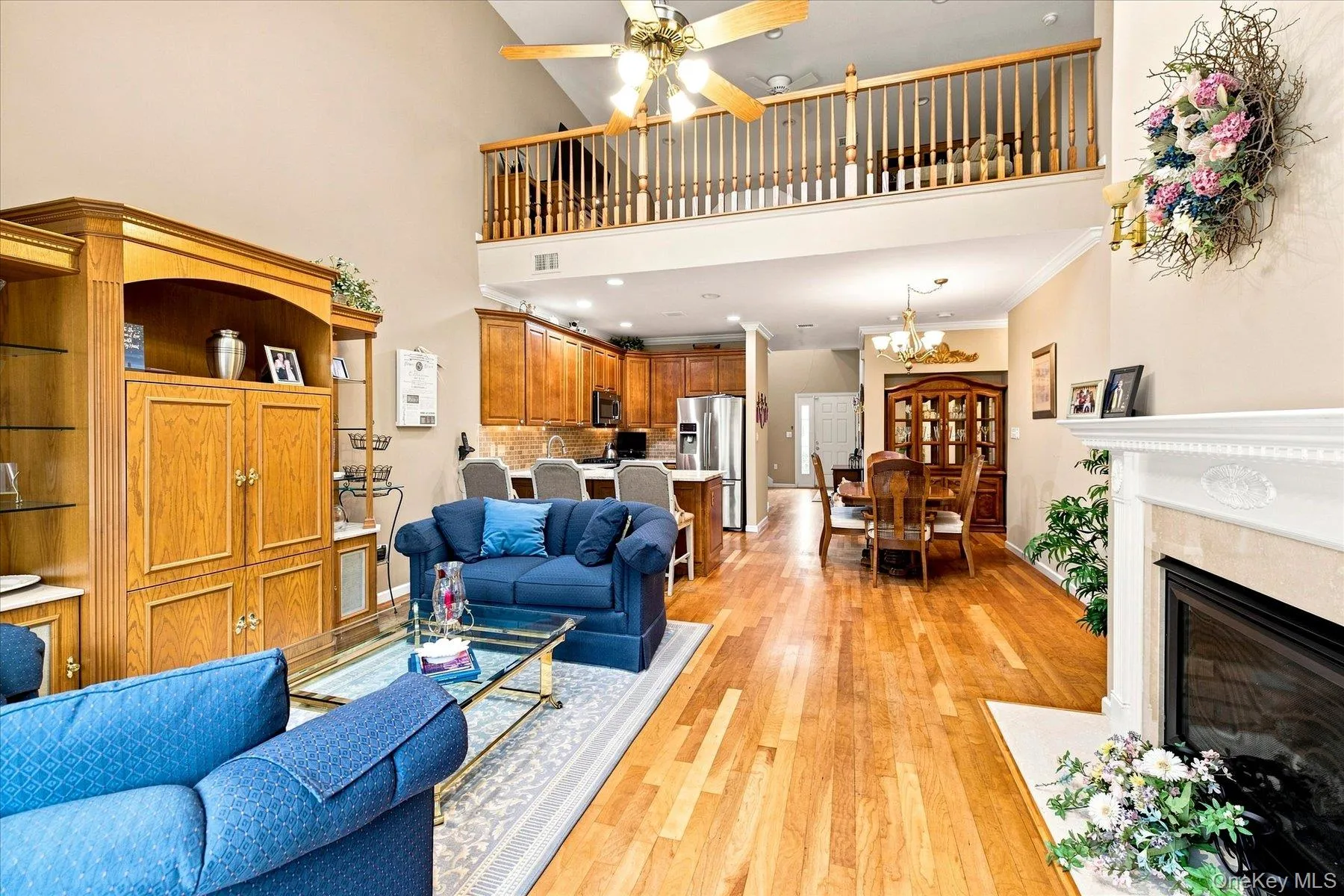 Two-story living area with wood-finish flooring, a white mantel fireplace, and a ceiling fan Two-story living area with wood-finish flooring, a white mantel fireplace, and a ceiling fan