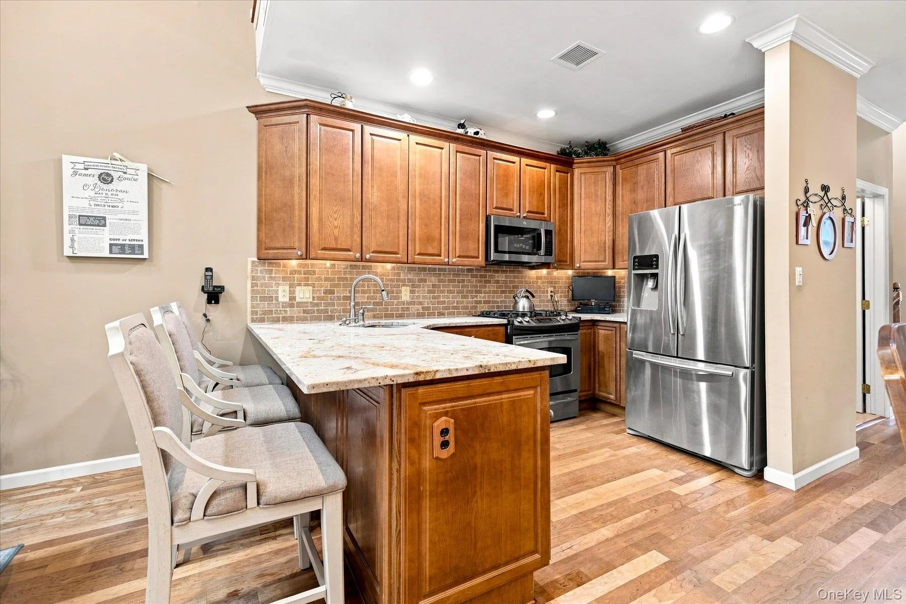 Wood-finish flooring with a U-shaped kitchen island featuring a granite-style countertop, stainless steel appliances, and wood cabinetry Wood-finish flooring with a U-shaped kitchen island featuring a granite-style countertop, stainless steel appliances, and wood cabinetry