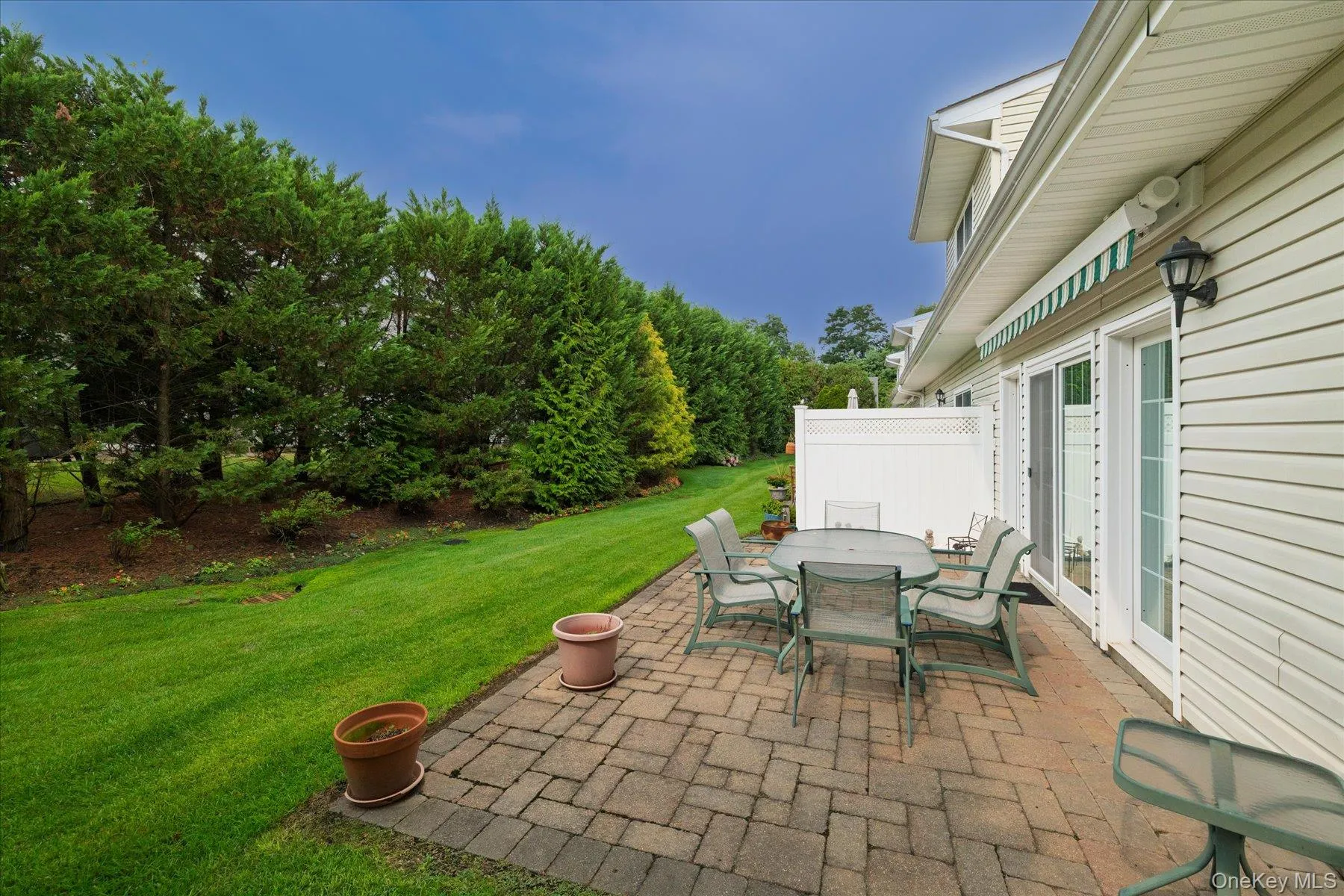 Expansive paver patio with a retractable awning, surrounded by a manicured lawn and mature privacy trees Expansive paver patio with a retractable awning, surrounded by a manicured lawn and mature privacy trees