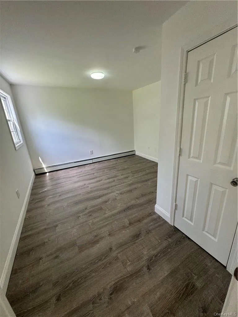 Spare room with dark wood-type flooring and baseboard heating Spare room with dark wood-type flooring and baseboard heating