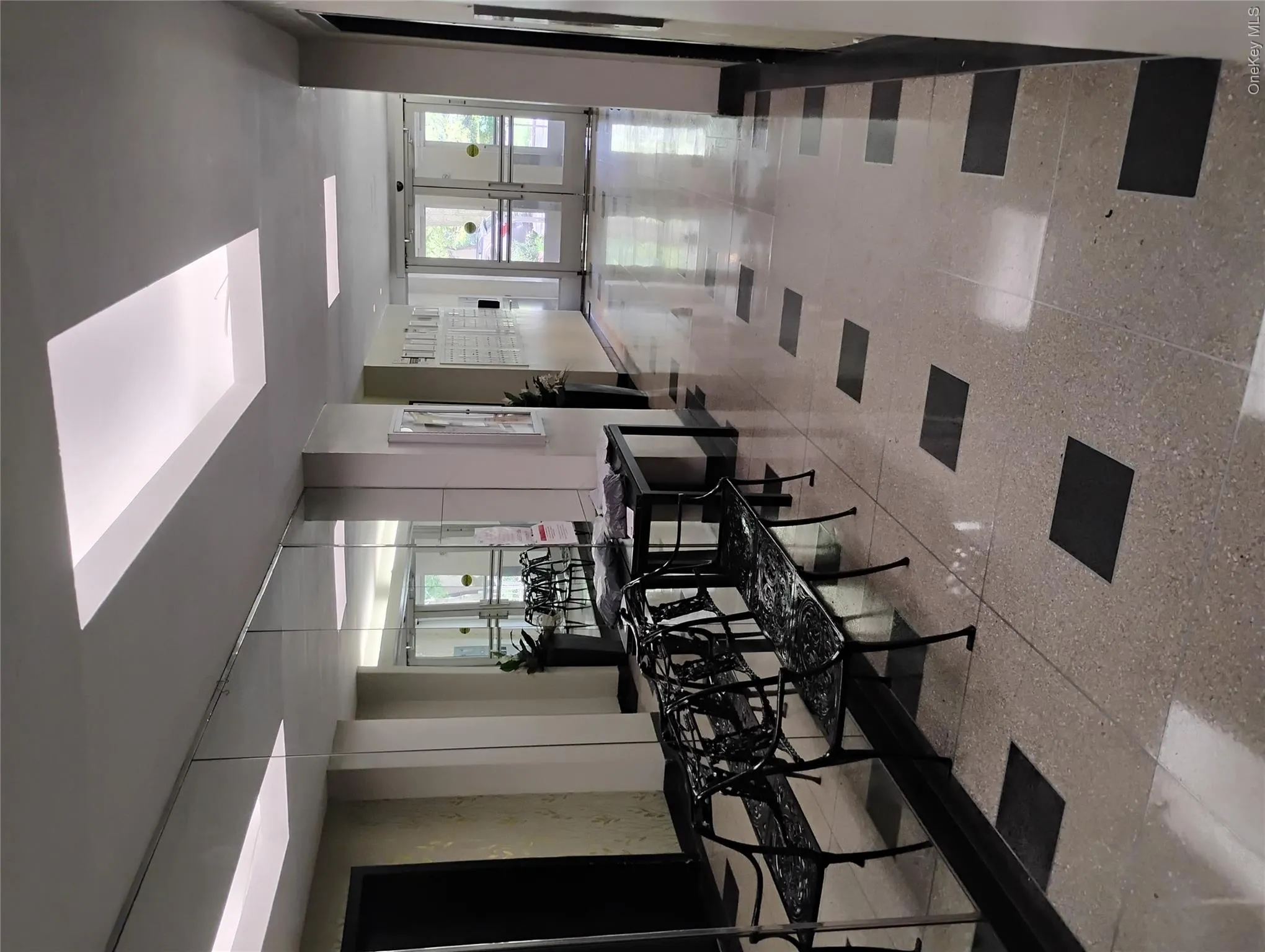 Terrazzo flooring with black tile accents, full-wall mirrored panels, double glass entry doors, and recessed ceiling lighting Terrazzo flooring with black tile accents, full-wall mirrored panels, double glass entry doors, and recessed ceiling lighting