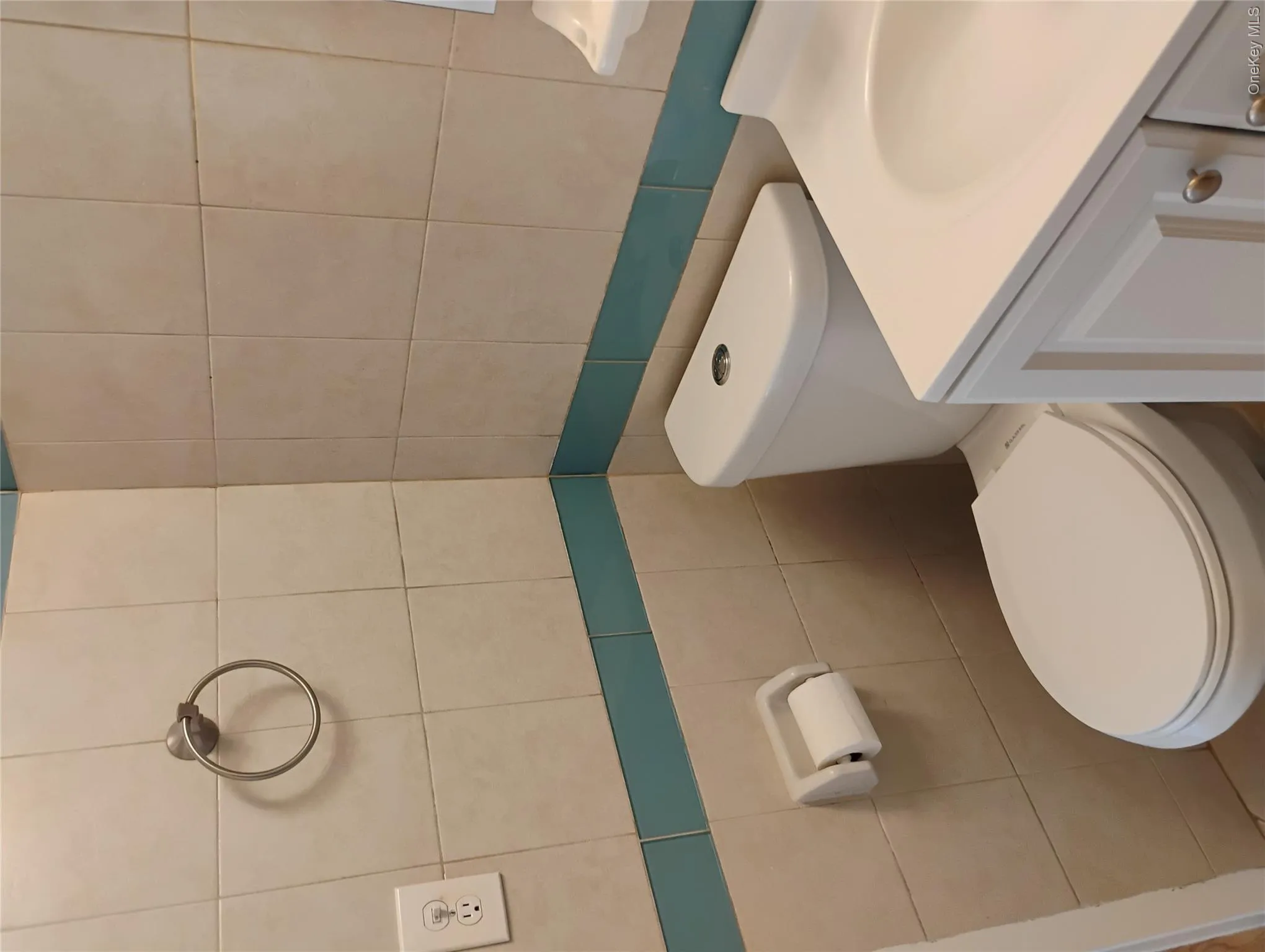 White ceramic tile walls with a teal accent band, white toilet, and white vanity with an integrated sink White ceramic tile walls with a teal accent band, white toilet, and white vanity with an integrated sink