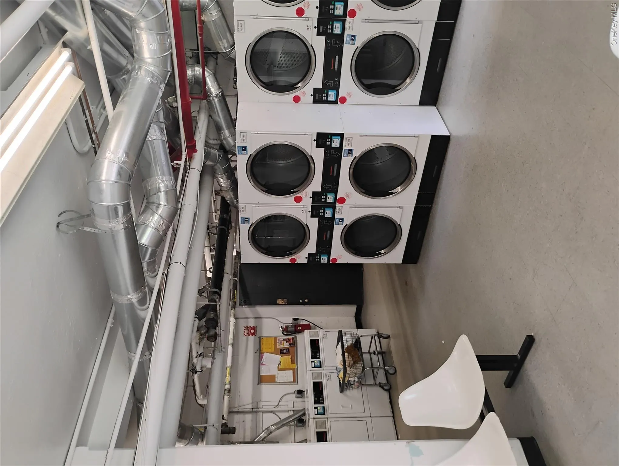 Communal laundry facility featuring multiple commercial-grade washers and dryers, exposed ceiling ductwork, and concrete flooring Communal laundry facility featuring multiple commercial-grade washers and dryers, exposed ceiling ductwork, and concrete flooring