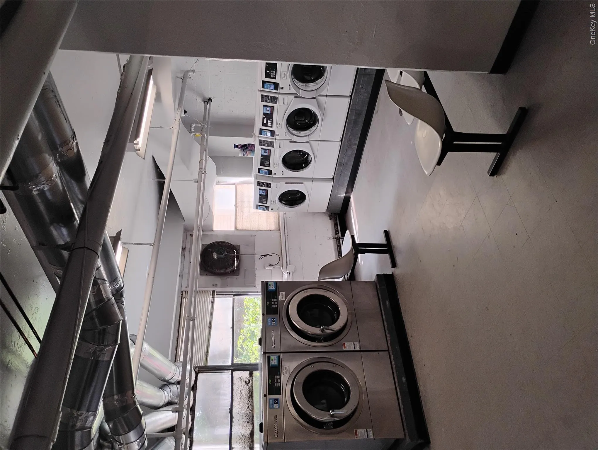 Laundry facility featuring multiple washers and dryers, exposed ceiling ductwork, and fluorescent lighting Laundry facility featuring multiple washers and dryers, exposed ceiling ductwork, and fluorescent lighting