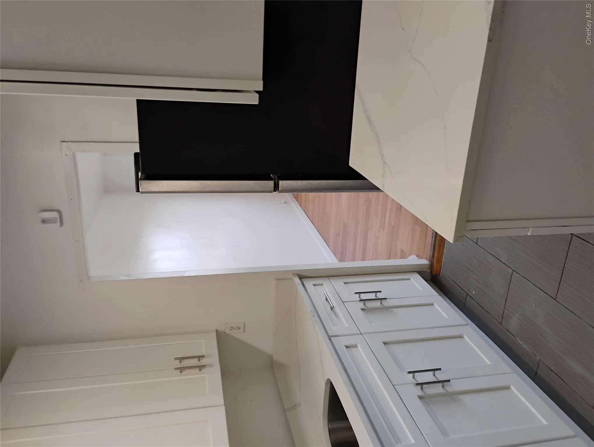 White shaker-style cabinetry with matte black hardware, light-toned countertops, stainless steel sink, and gray tile flooring White shaker-style cabinetry with matte black hardware, light-toned countertops, stainless steel sink, and gray tile flooring
