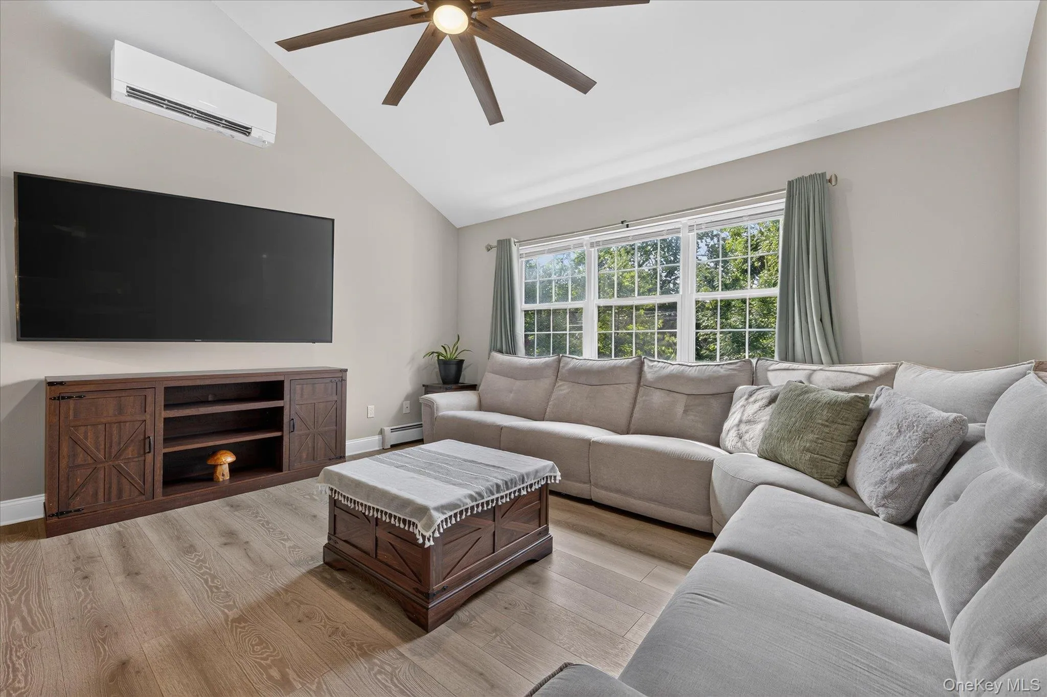 Vaulted ceiling with a ceiling fan, wall-mounted climate control unit, wood-finish flooring, and large multi-pane windows Vaulted ceiling with a ceiling fan, wall-mounted climate control unit, wood-finish flooring, and large multi-pane windows
