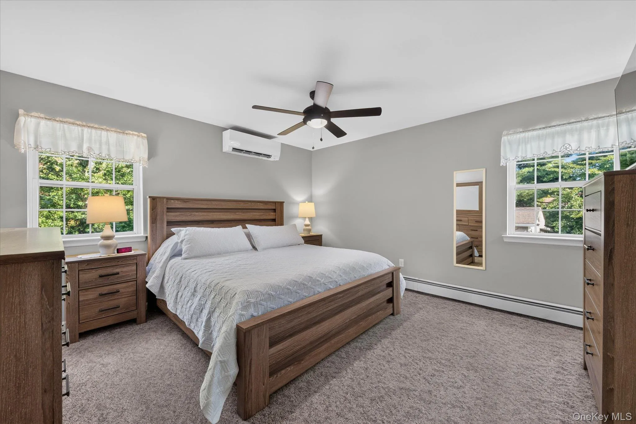 Carpeted room with a ceiling fan, two windows, and a wall-mounted climate control unit Carpeted room with a ceiling fan, two windows, and a wall-mounted climate control unit