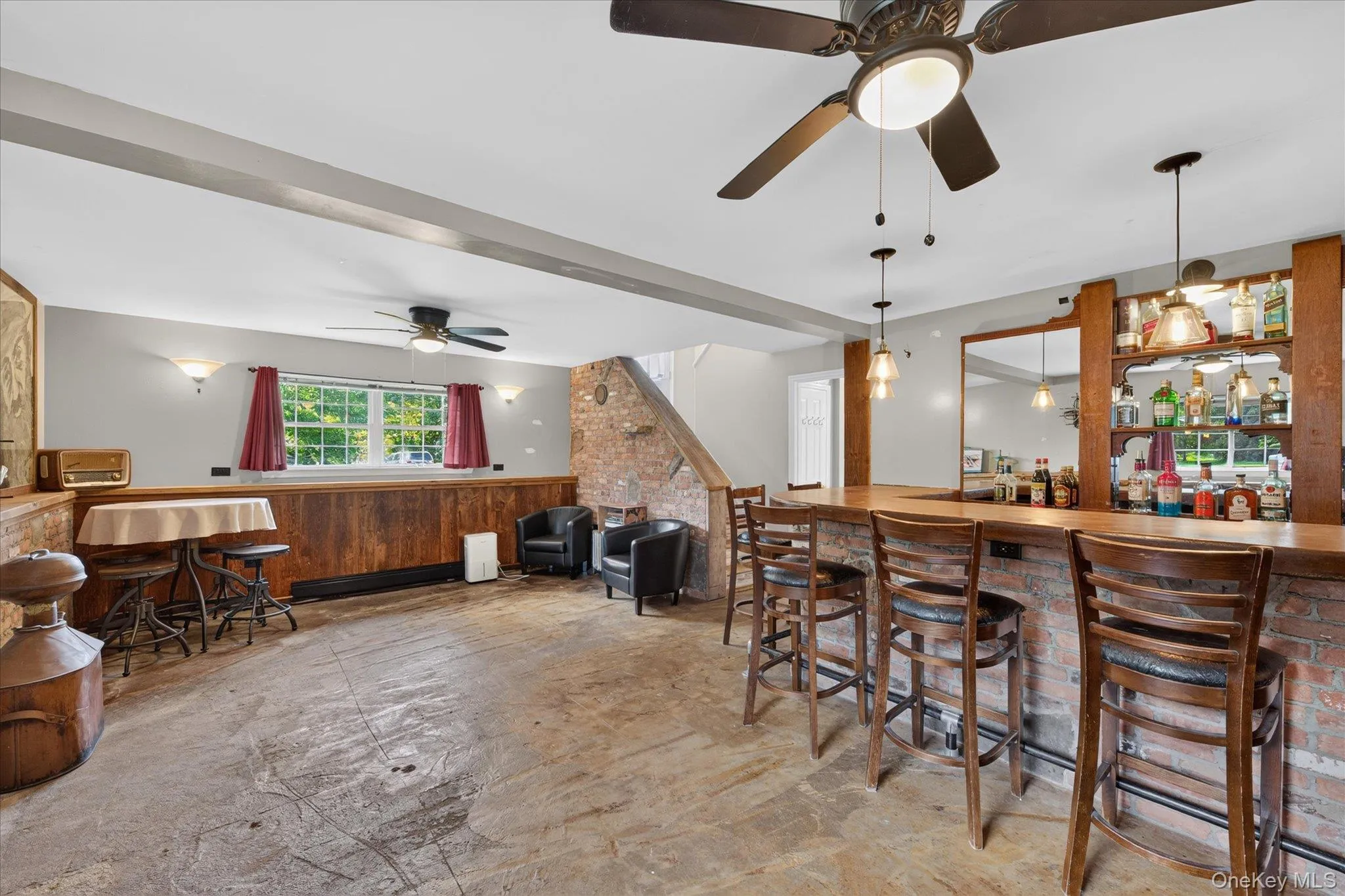 Finished lower level featuring a built-in bar with brick detailing, wood-finish flooring, two ceiling fans, and sconce lighting Finished lower level featuring a built-in bar with brick detailing, wood-finish flooring, two ceiling fans, and sconce lighting