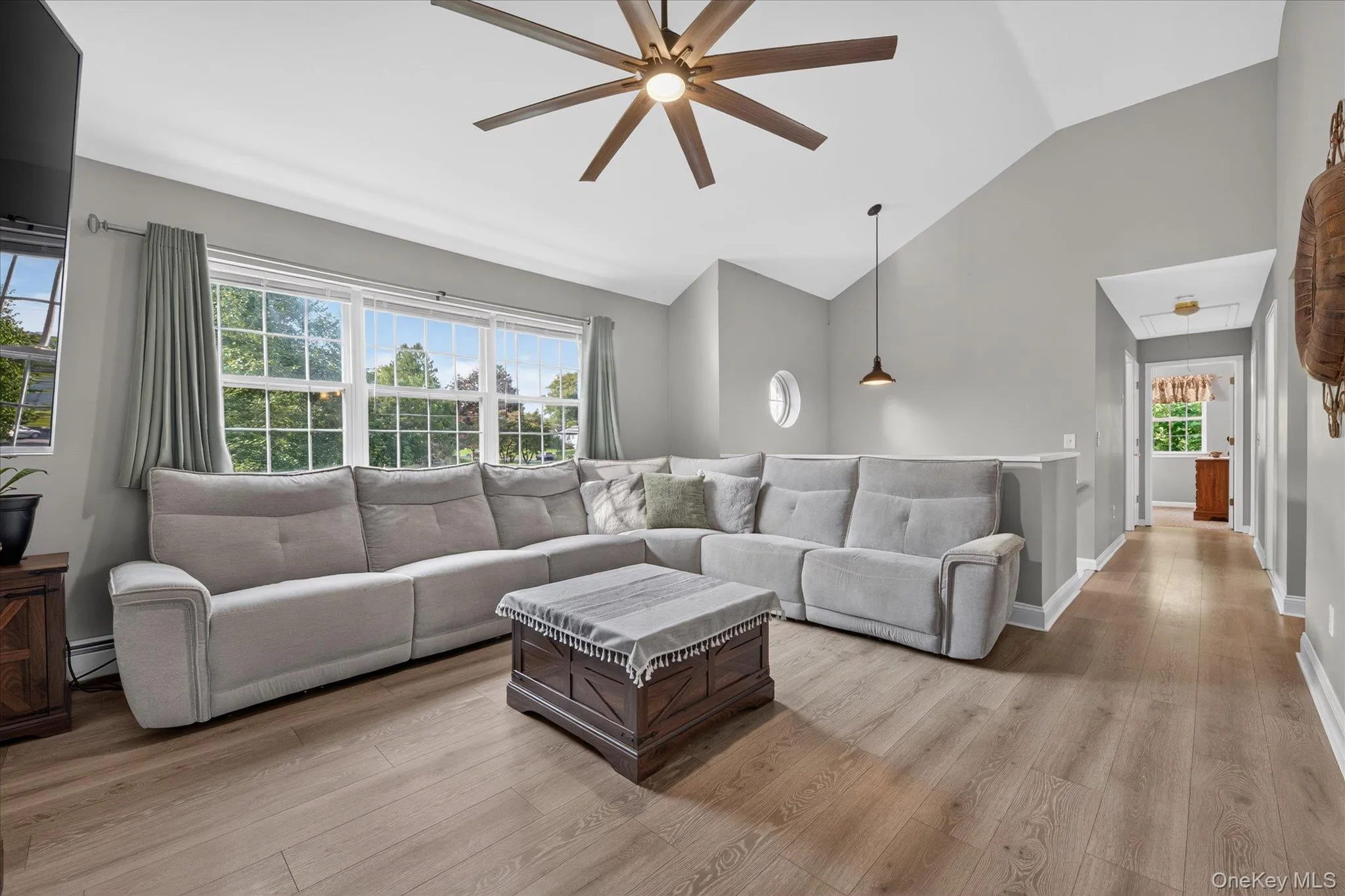 Vaulted ceiling with an integrated ceiling fan, wood-finish flooring, and a large window array Vaulted ceiling with an integrated ceiling fan, wood-finish flooring, and a large window array