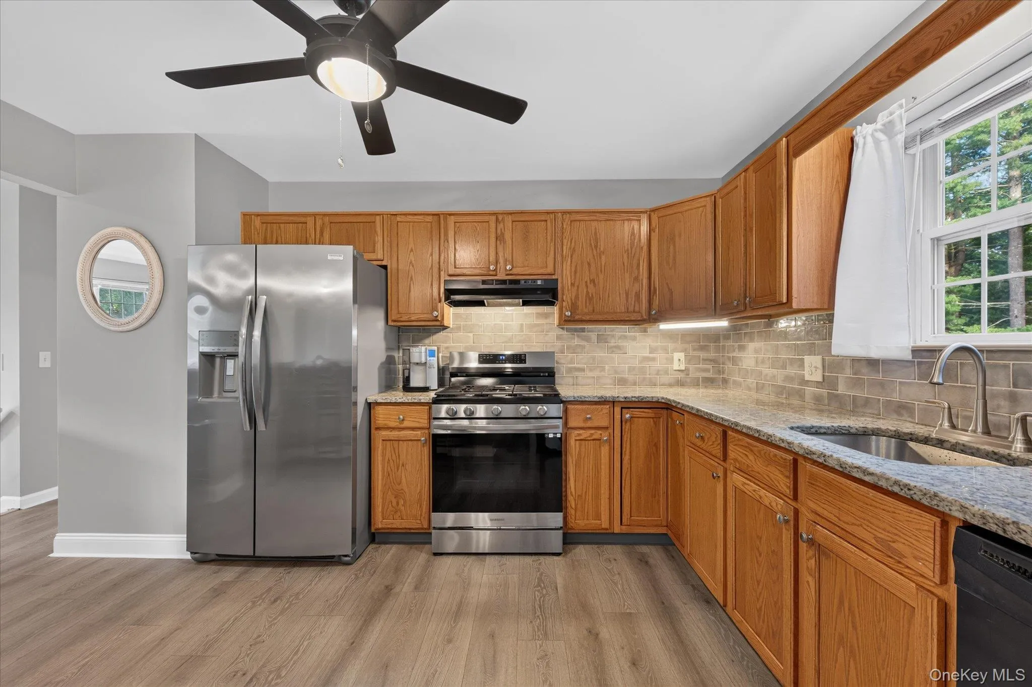 Kitchen featuring wood-finish cabinetry, stainless steel appliances, speckled countertops, tile backsplash, and wood-finish flooring Kitchen featuring wood-finish cabinetry, stainless steel appliances, speckled countertops, tile backsplash, and wood-finish flooring