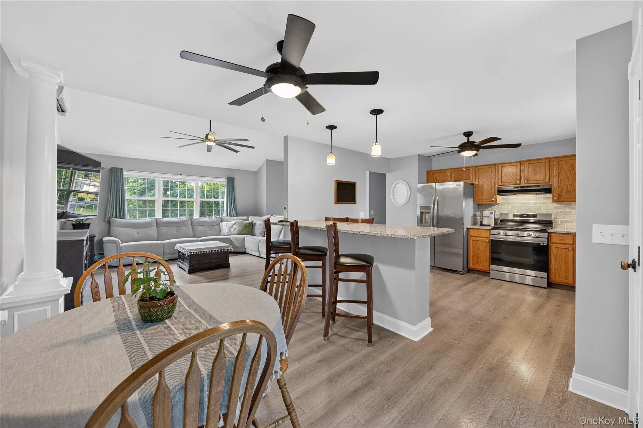 Open-concept living area with wood-finish flooring, a kitchen island with seating, pendant lighting, and stainless steel appliances Open-concept living area with wood-finish flooring, a kitchen island with seating, pendant lighting, and stainless steel appliances