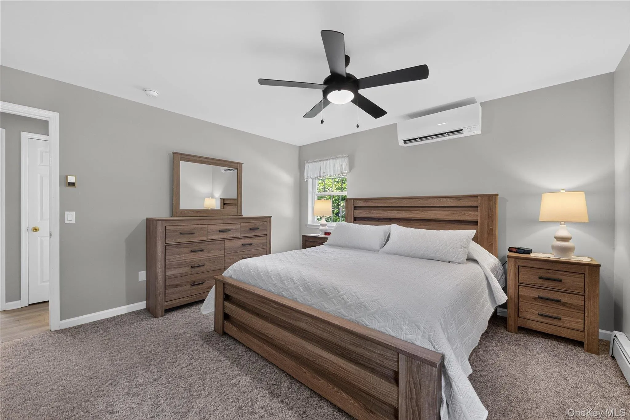 Wall-mounted air conditioning unit, ceiling fan with integrated lighting, window with natural light, and plush carpeting Wall-mounted air conditioning unit, ceiling fan with integrated lighting, window with natural light, and plush carpeting