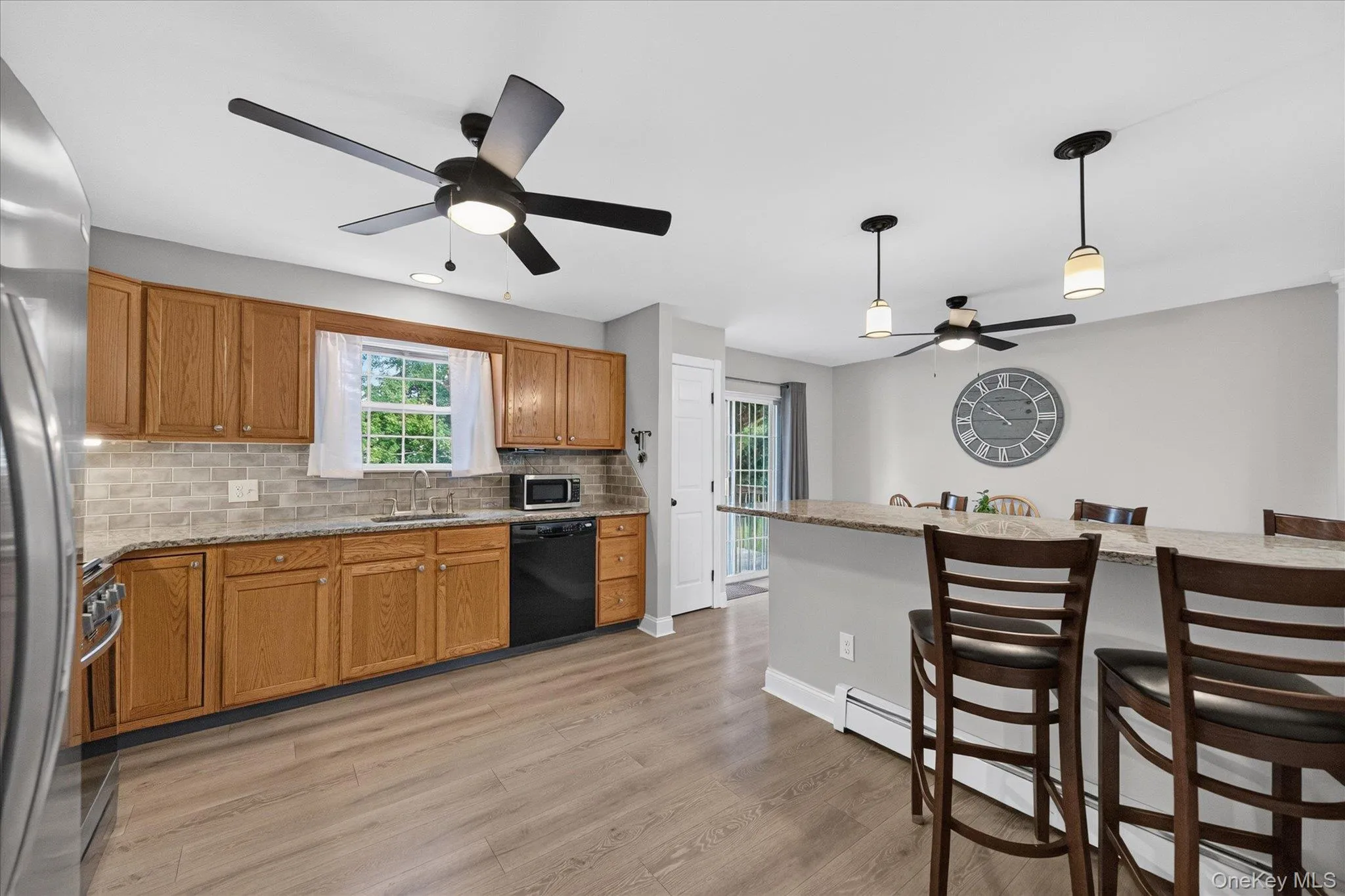 Kitchen featuring wood-finish flooring, wood cabinetry, stone-finish countertops, tiled backsplash, and recessed lighting Kitchen featuring wood-finish flooring, wood cabinetry, stone-finish countertops, tiled backsplash, and recessed lighting