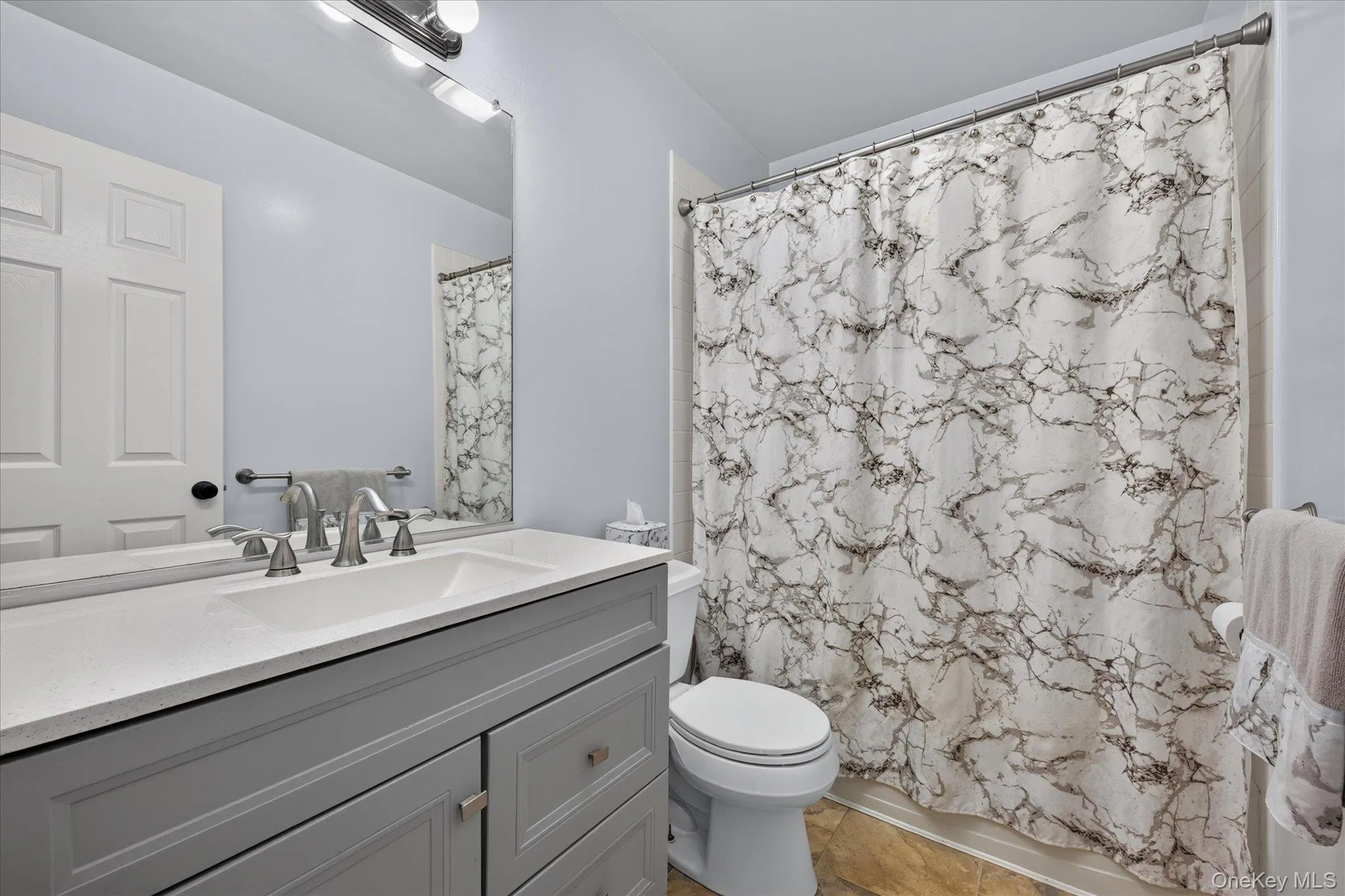 Gray vanity with integrated sink, brushed nickel faucet, large vanity mirror, and wood-finish flooring Gray vanity with integrated sink, brushed nickel faucet, large vanity mirror, and wood-finish flooring