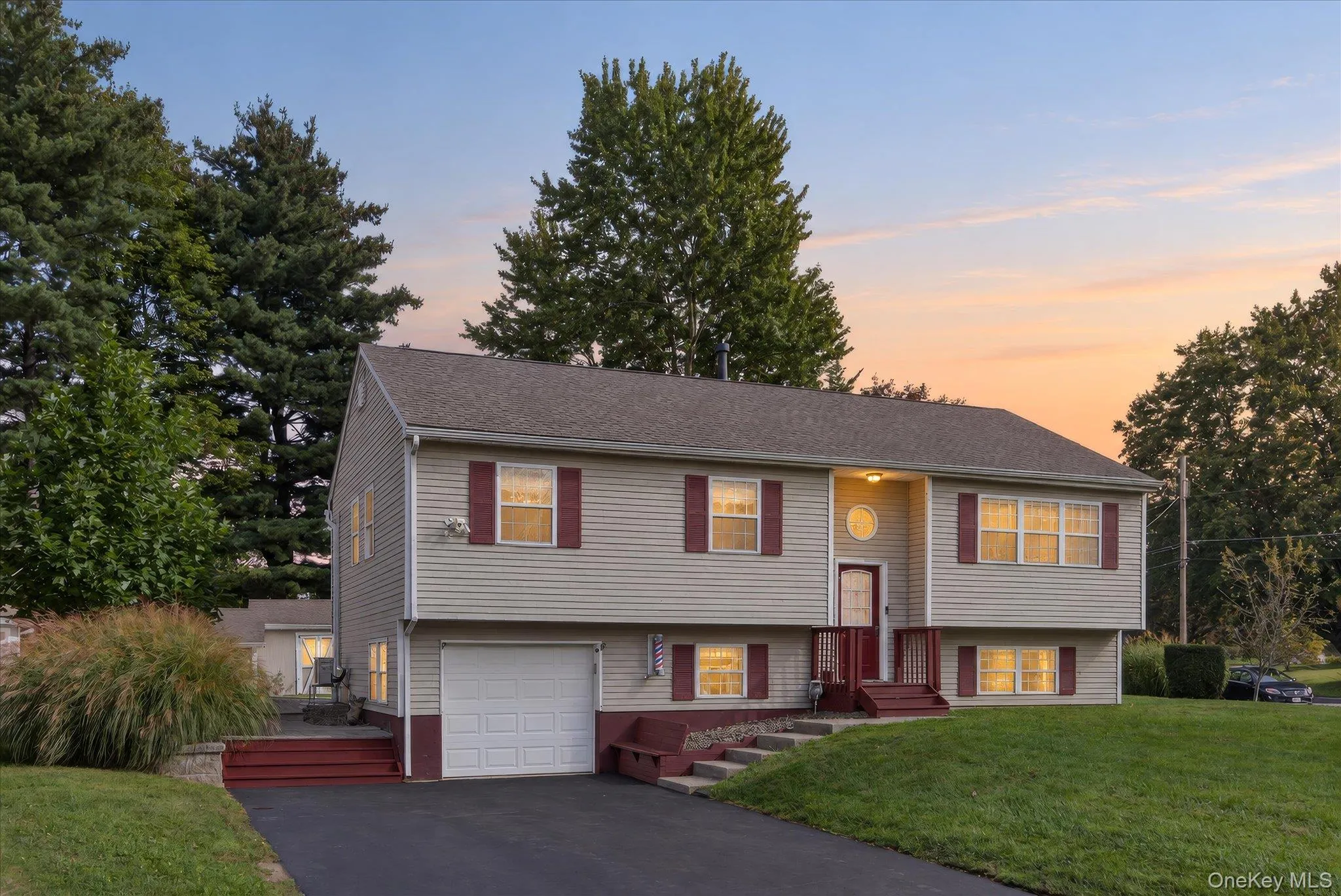 Split-level residence featuring light-colored siding, a dark asphalt shingle roof, and a red-painted front entry and stairs Split-level residence featuring light-colored siding, a dark asphalt shingle roof, and a red-painted front entry and stairs