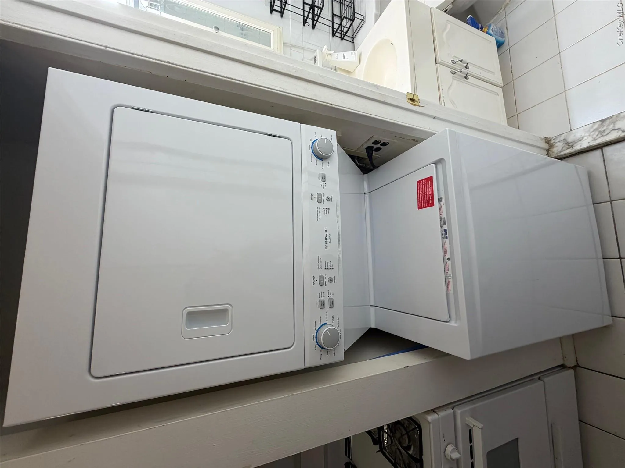 Laundry room with stacked washer / drying machine and light tile patterned floors Laundry room with stacked washer / drying machine and light tile patterned floors