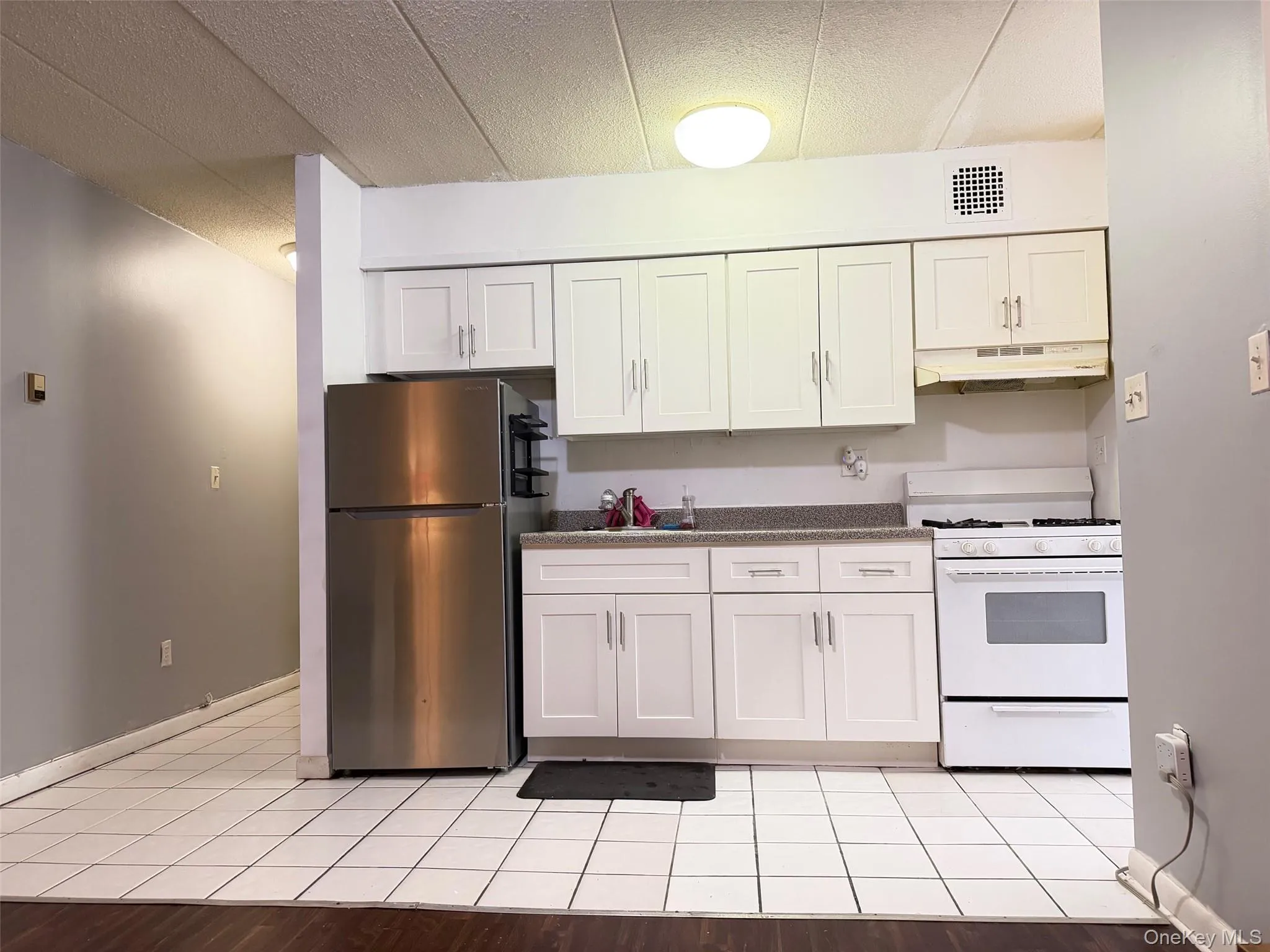 Kitchen with white range with gas cooktop, freestanding refrigerator, white cabinets, under cabinet range hood, and light tile patterned flooring Kitchen with white range with gas cooktop, freestanding refrigerator, white cabinets, under cabinet range hood, and light tile patterned flooring