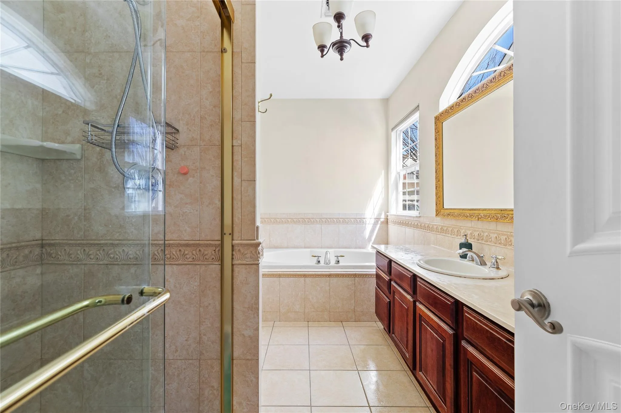 Tiled shower enclosure with a glass door, built-in bathtub, dual windows, and a vanity with an integrated sink and wood-finish cabinetry Tiled shower enclosure with a glass door, built-in bathtub, dual windows, and a vanity with an integrated sink and wood-finish cabinetry