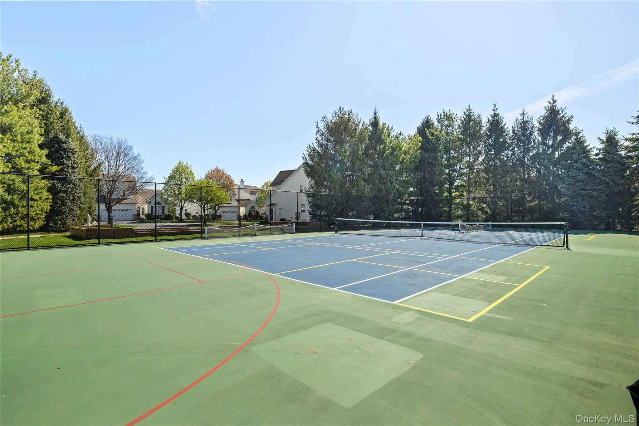 Full-sized tennis court with a perimeter fence, surrounded by mature trees Full-sized tennis court with a perimeter fence, surrounded by mature trees