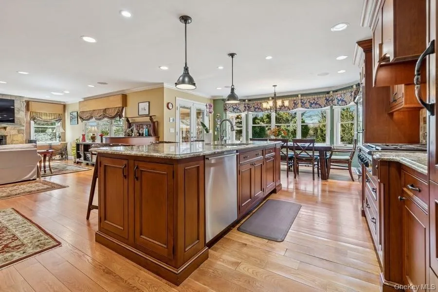 Chef's kitchen showcasing rich wood cabinetry, a large center island with stone countertops, stainless steel appliances, pendant lighting, hardwood flooring, and abundant natural light from multiple windows overlooking the grounds Chef's kitchen showcasing rich wood cabinetry, a large center island with stone countertops, stainless steel appliances, pendant lighting, hardwood flooring, and abundant natural light from multiple windows overlooking the grounds
