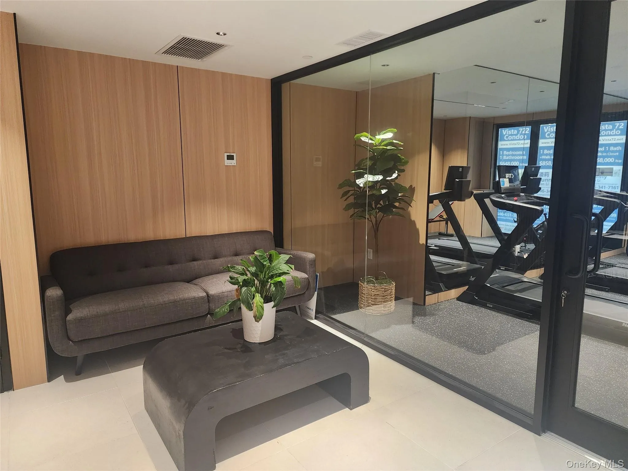 Wood-paneled wall, white ceiling, recessed lighting, white flooring, and glass wall Wood-paneled wall, white ceiling, recessed lighting, white flooring, and glass wall