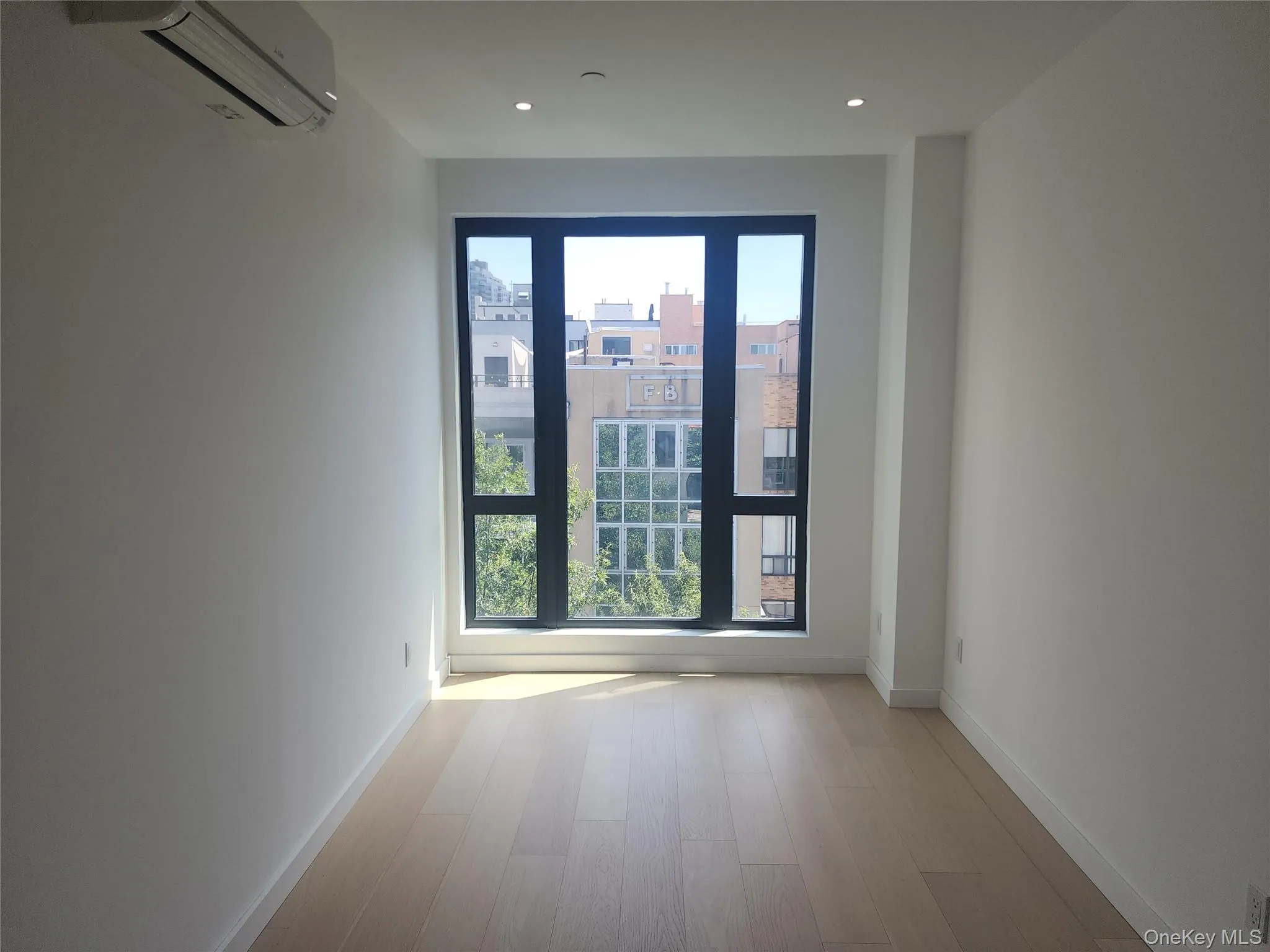 Recessed ceiling lighting, full-height window, wood-finish flooring, white walls, and a wall-mounted air conditioning unit Recessed ceiling lighting, full-height window, wood-finish flooring, white walls, and a wall-mounted air conditioning unit