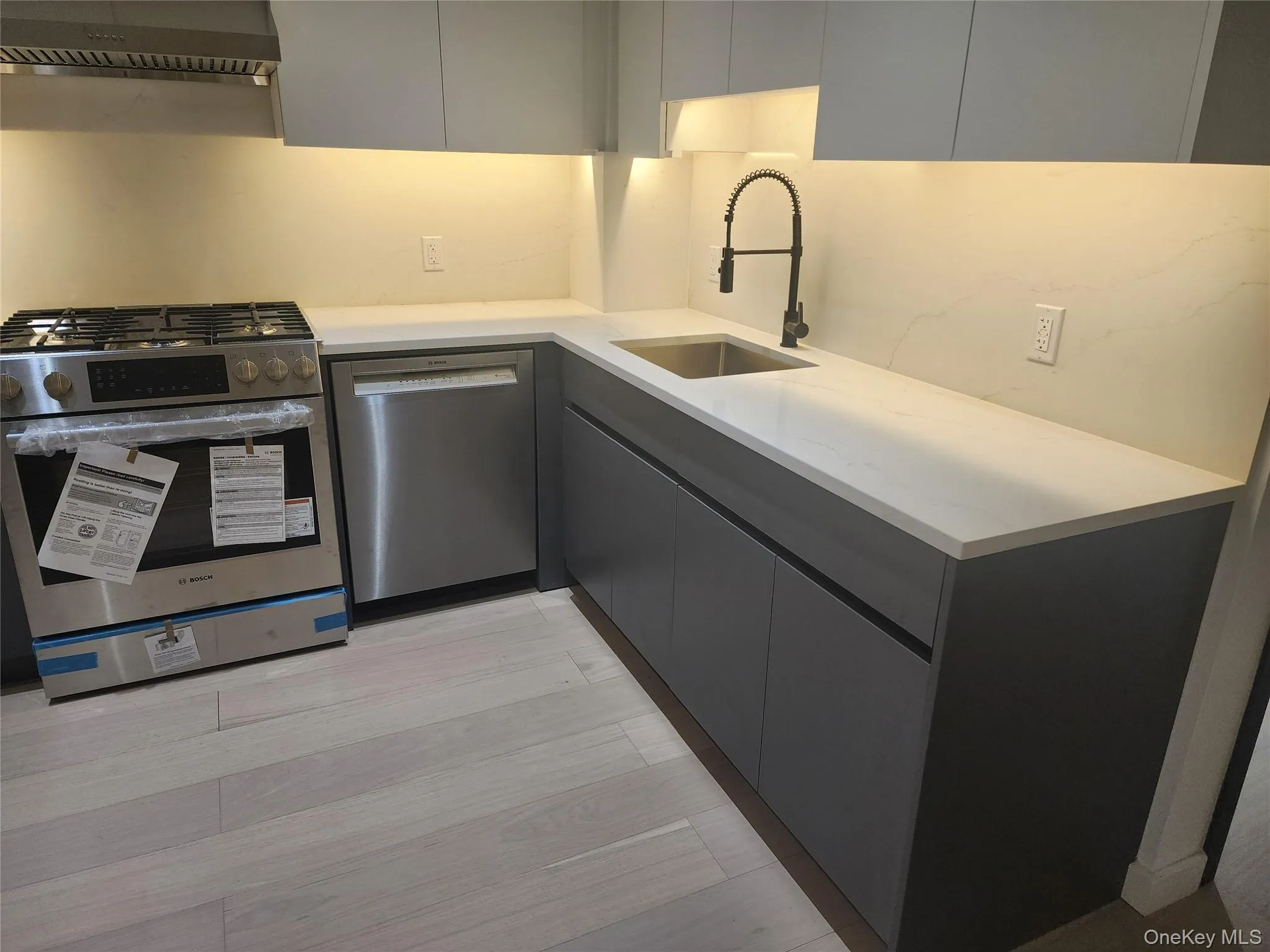 Modern kitchen featuring light wood-finish flooring, stainless steel appliances, white countertops, and gray cabinetry Modern kitchen featuring light wood-finish flooring, stainless steel appliances, white countertops, and gray cabinetry