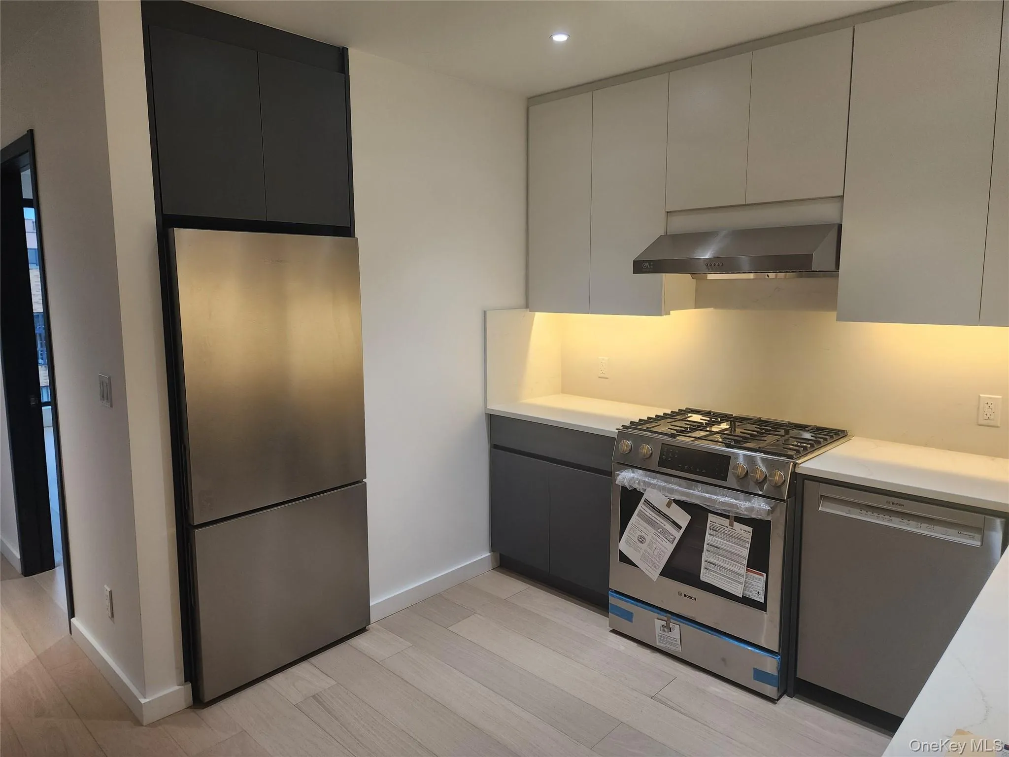 Stainless steel appliance suite, light wood-finish flooring, white countertops, gray upper cabinetry, and dark gray lower cabinetry Stainless steel appliance suite, light wood-finish flooring, white countertops, gray upper cabinetry, and dark gray lower cabinetry