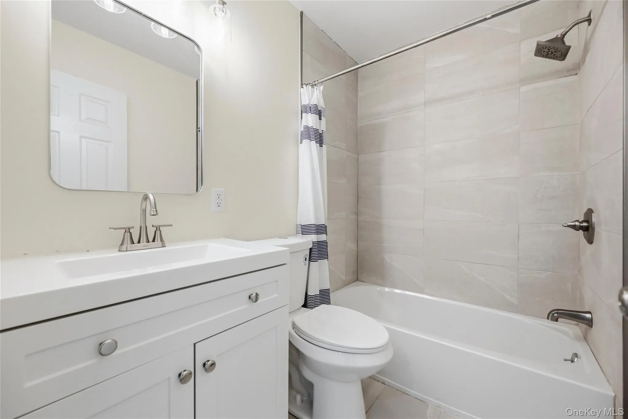 White vanity with integrated sink, brushed nickel faucet, large mirror, tile shower surround, and white bathtub White vanity with integrated sink, brushed nickel faucet, large mirror, tile shower surround, and white bathtub