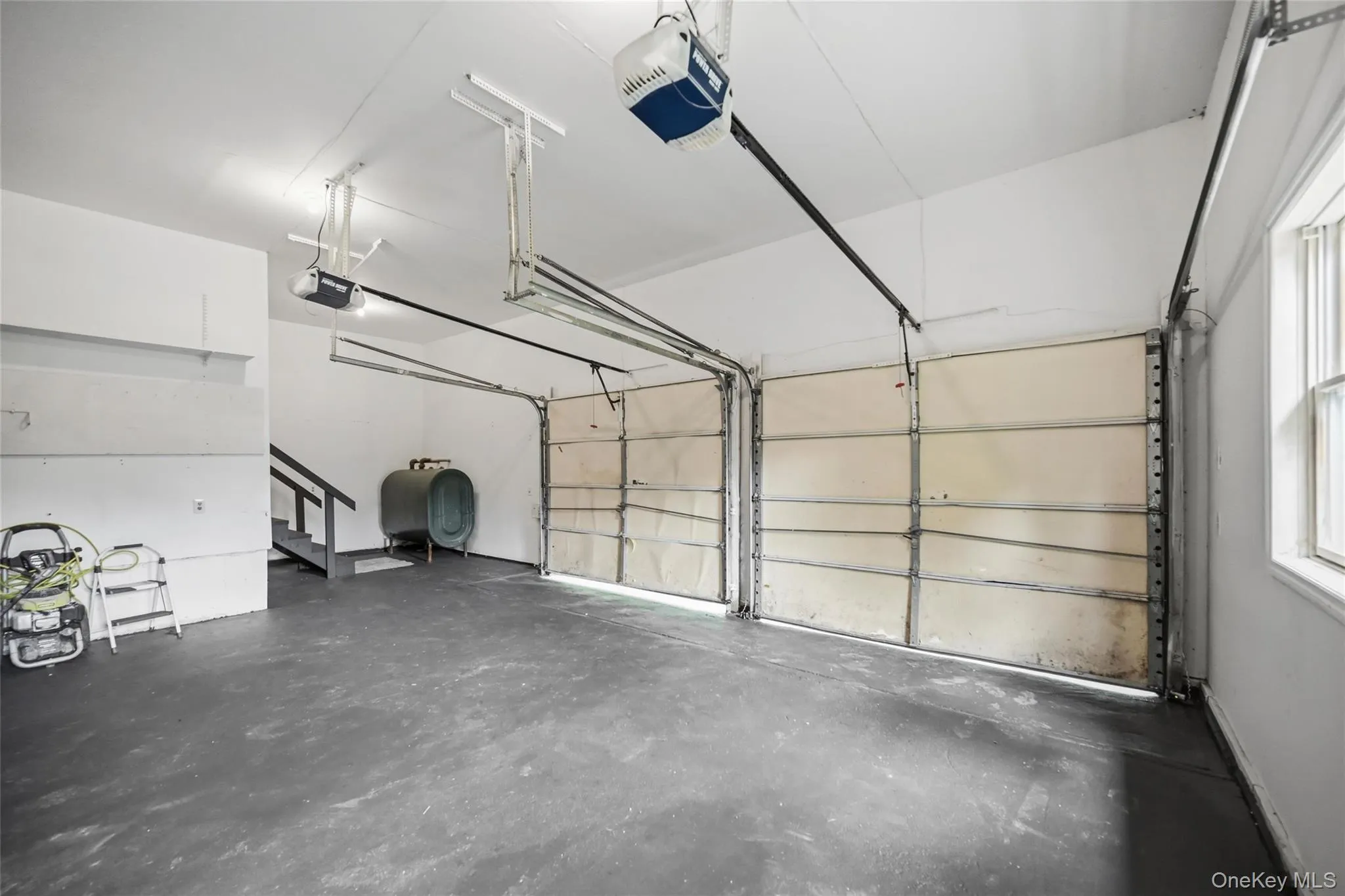 Two-car garage with concrete flooring, two overhead garage doors, and a staircase Two-car garage with concrete flooring, two overhead garage doors, and a staircase