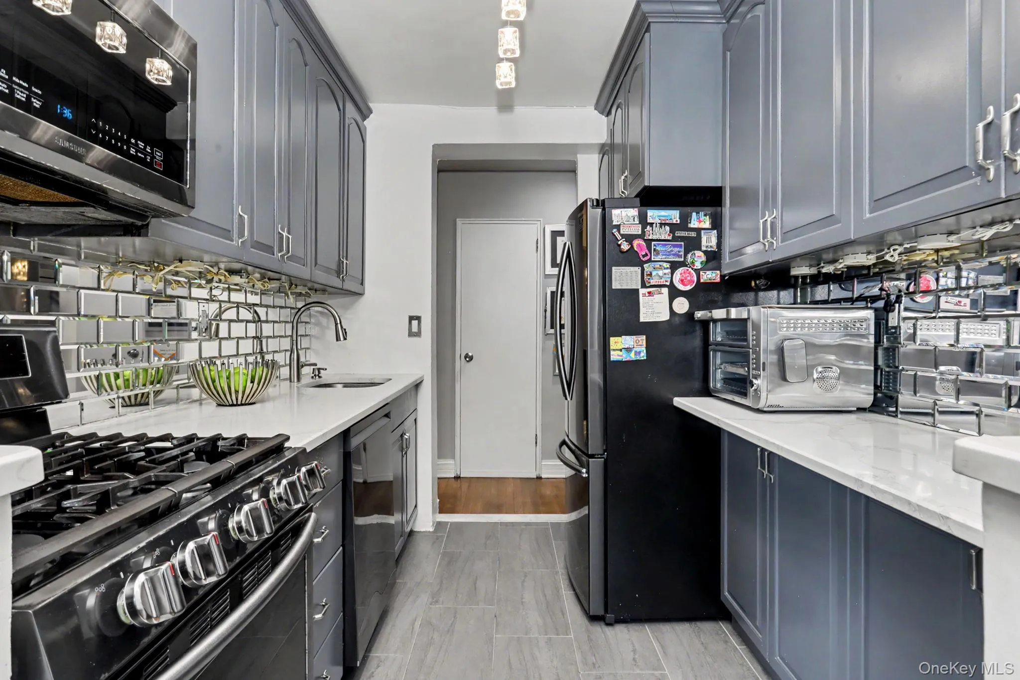 Galley kitchen featuring gray cabinetry, white countertops, stainless steel appliances, and a mirrored subway tile backsplash Galley kitchen featuring gray cabinetry, white countertops, stainless steel appliances, and a mirrored subway tile backsplash