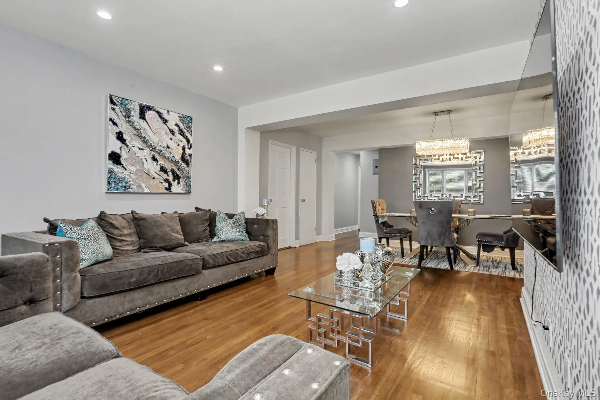 Hardwood flooring, recessed ceiling lighting, textured accent wall, and a dining area featuring a chandelier Hardwood flooring, recessed ceiling lighting, textured accent wall, and a dining area featuring a chandelier