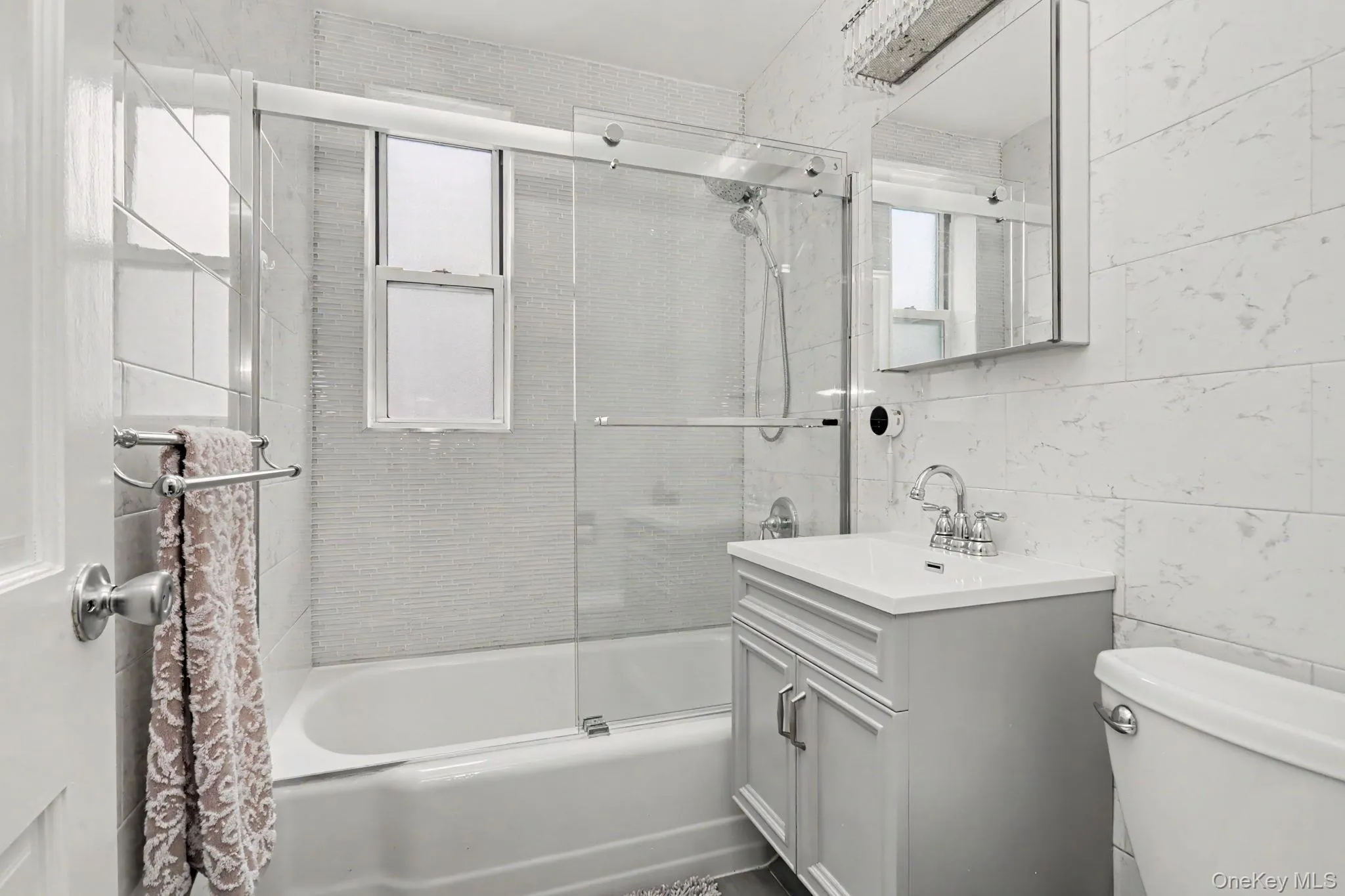 Tiled shower with glass sliding doors, gray vanity with integrated sink, chrome fixtures, and a mirrored medicine cabinet Tiled shower with glass sliding doors, gray vanity with integrated sink, chrome fixtures, and a mirrored medicine cabinet