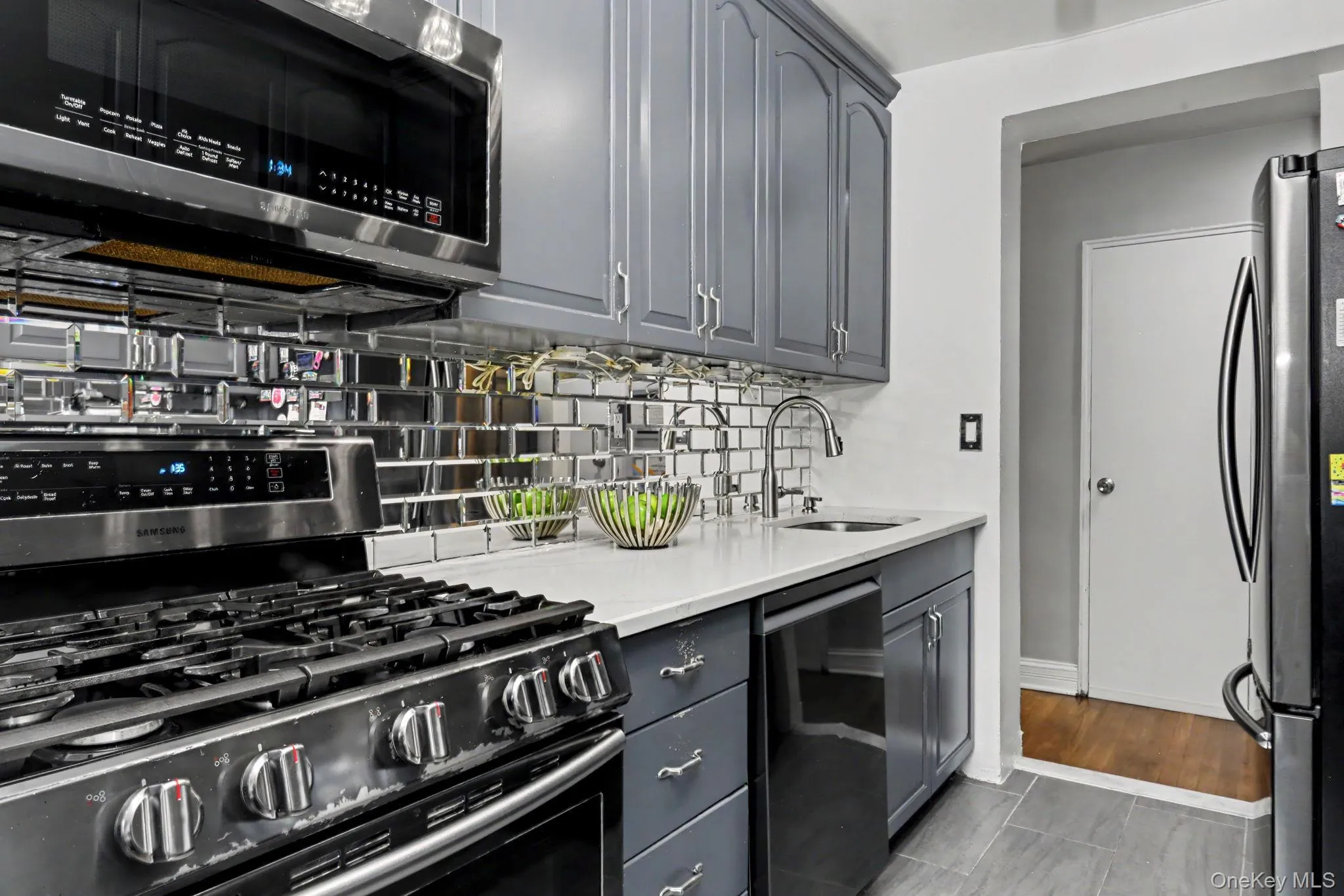 Stainless steel appliance suite, gray shaker-style cabinetry, mirrored subway tile backsplash, white countertop, and a stainless steel sink with a gooseneck faucet Stainless steel appliance suite, gray shaker-style cabinetry, mirrored subway tile backsplash, white countertop, and a stainless steel sink with a gooseneck faucet