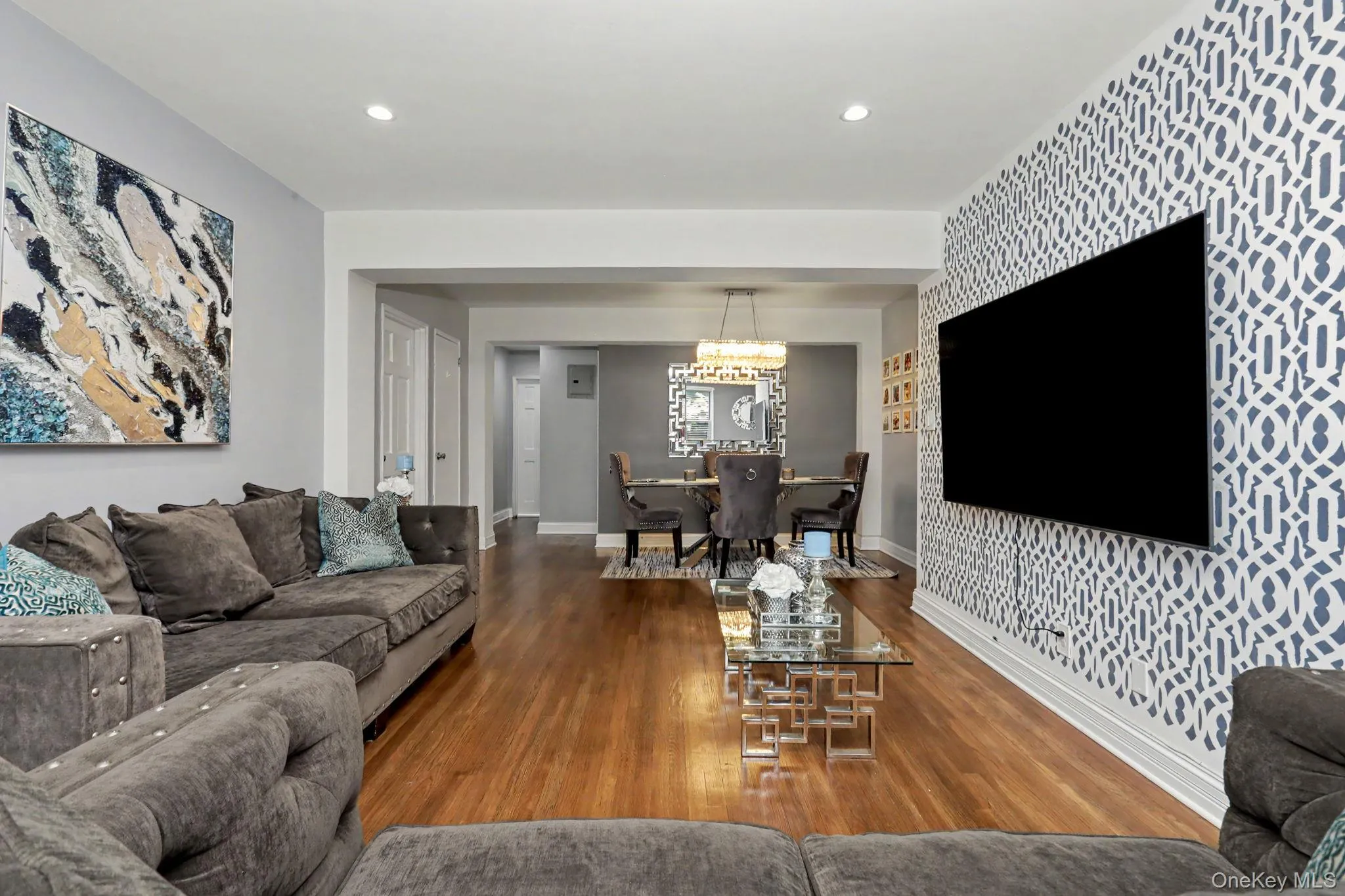 Hardwood flooring throughout, recessed lighting, accent wall with geometric pattern, and a dining area with a chandelier Hardwood flooring throughout, recessed lighting, accent wall with geometric pattern, and a dining area with a chandelier