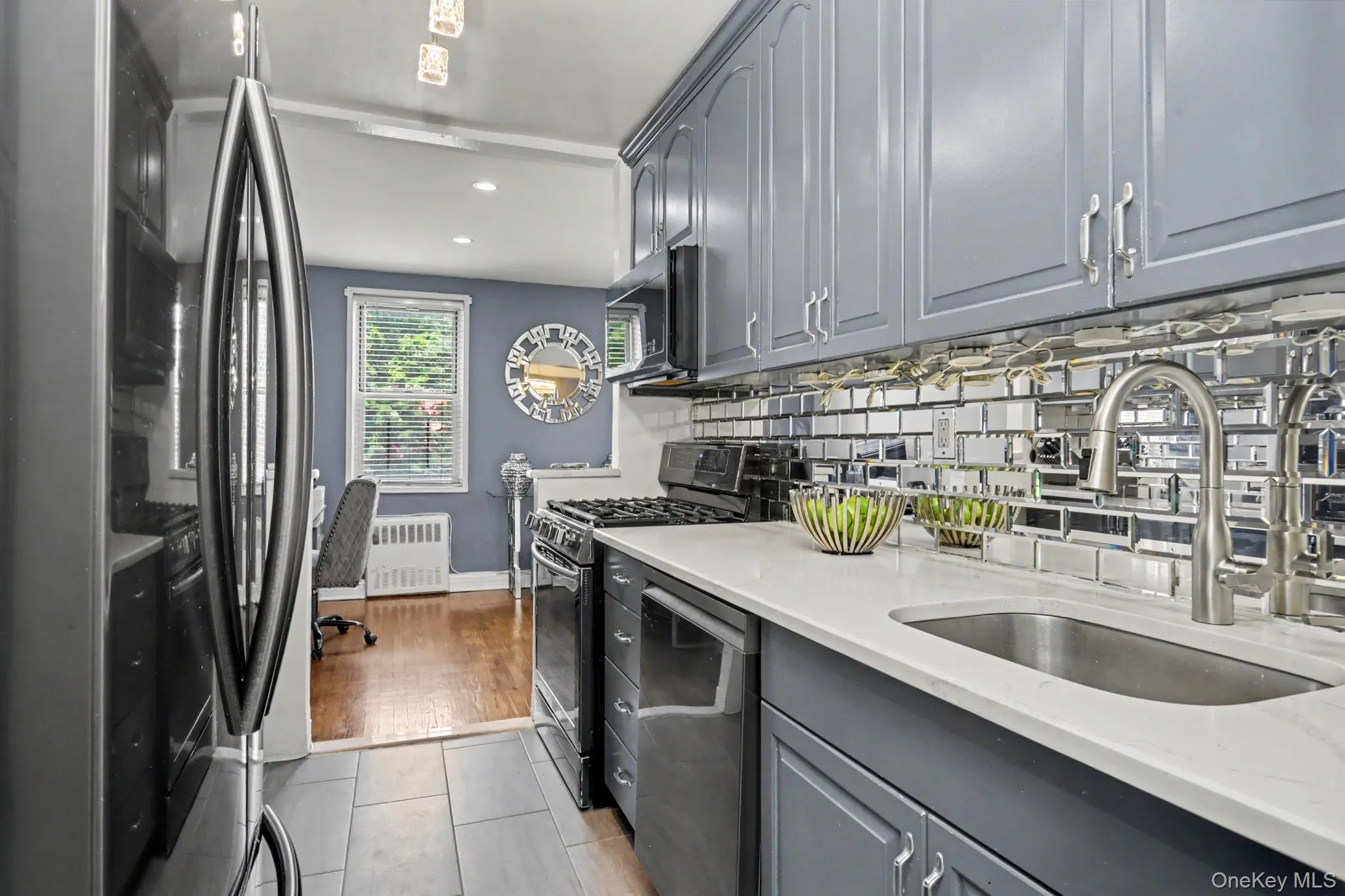 Stainless steel appliances, gray cabinetry, mirrored subway tile backsplash, white countertops, and tile flooring Stainless steel appliances, gray cabinetry, mirrored subway tile backsplash, white countertops, and tile flooring
