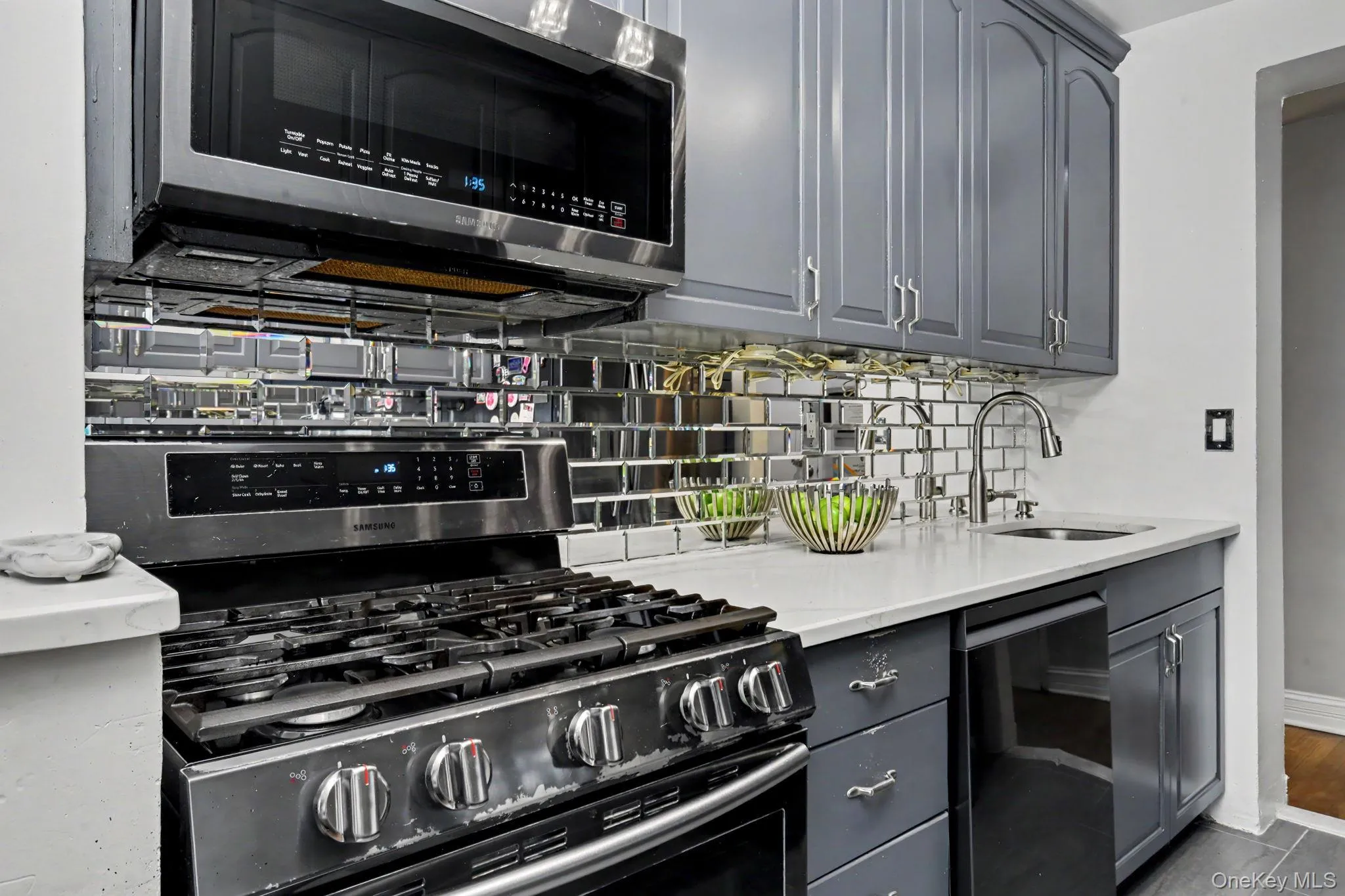 Stainless steel range with an over-the-range microwave, gray cabinetry with stainless steel hardware, mirrored subway tile backsplash, and a single basin sink with a gooseneck faucet Stainless steel range with an over-the-range microwave, gray cabinetry with stainless steel hardware, mirrored subway tile backsplash, and a single basin sink with a gooseneck faucet