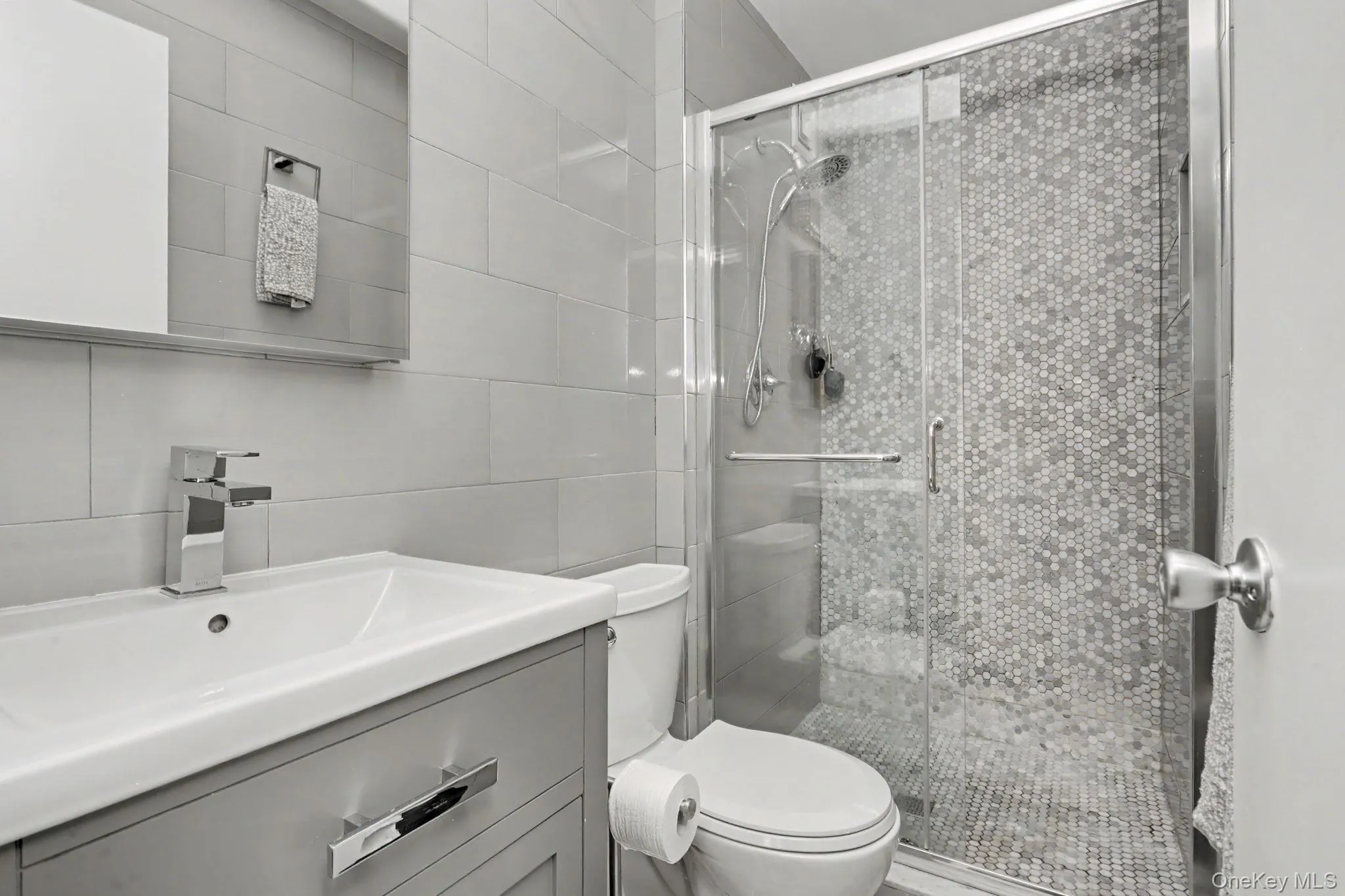 Bathroom featuring a glass-enclosed shower with mosaic tile, vanity with integrated sink, chrome faucet, and subway tile walls Bathroom featuring a glass-enclosed shower with mosaic tile, vanity with integrated sink, chrome faucet, and subway tile walls
