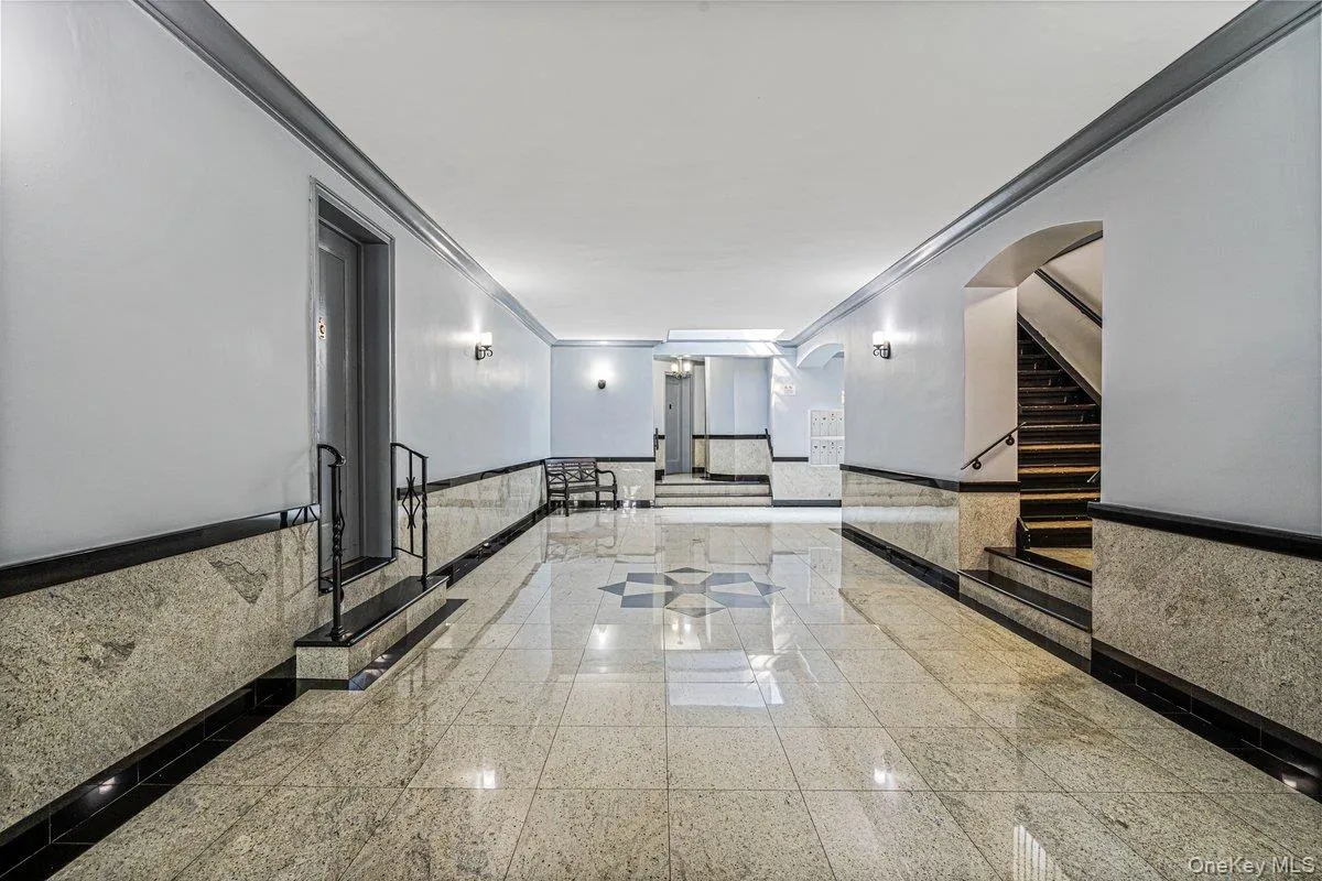 Polished stone tile flooring, stone wainscoting with dark trim, wall sconces, and a dedicated staircase Polished stone tile flooring, stone wainscoting with dark trim, wall sconces, and a dedicated staircase