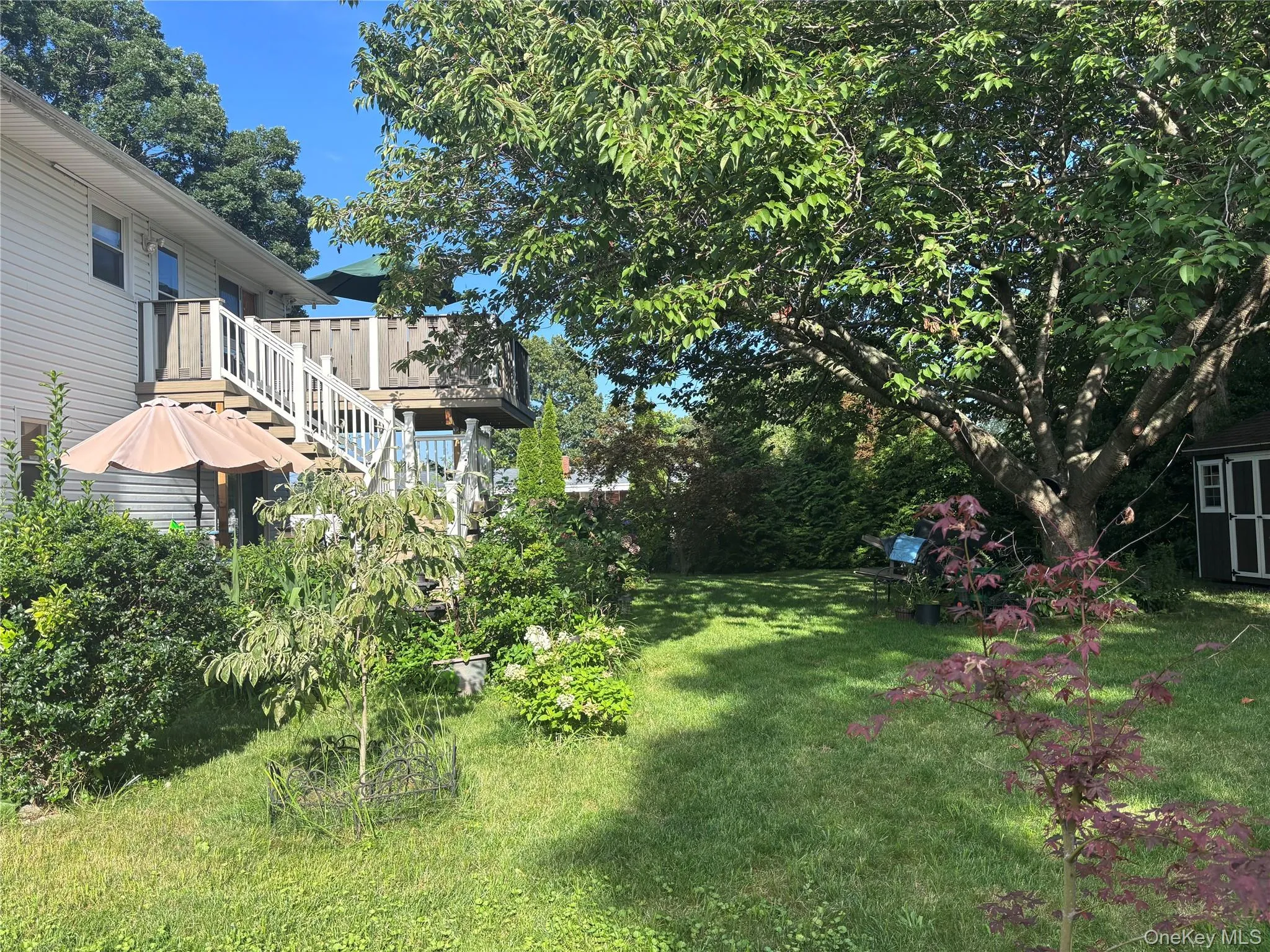 Expansive backyard featuring a large tree, a detached shed, and a two-story deck with white railings Expansive backyard featuring a large tree, a detached shed, and a two-story deck with white railings