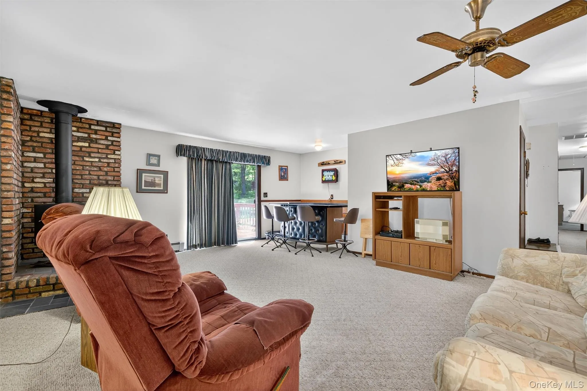 Carpeted living area with a wood stove, a ceiling fan, and a bar Carpeted living area with a wood stove, a ceiling fan, and a bar