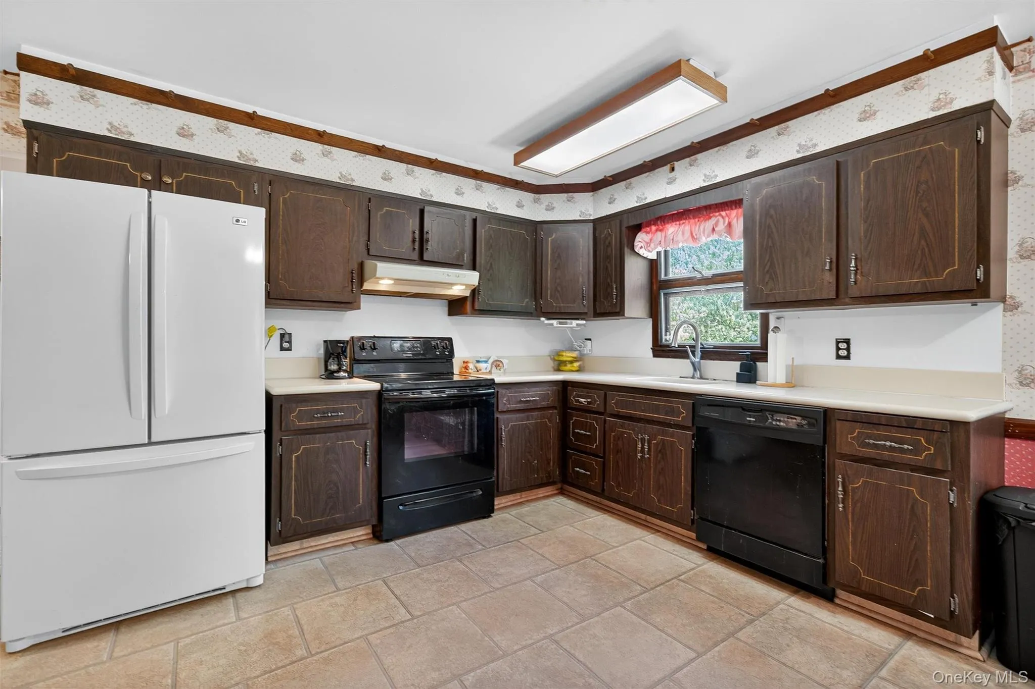 Kitchen featuring black appliances, under cabinet range hood, dark brown cabinets, wallpapered walls, and light countertops Kitchen featuring black appliances, under cabinet range hood, dark brown cabinets, wallpapered walls, and light countertops