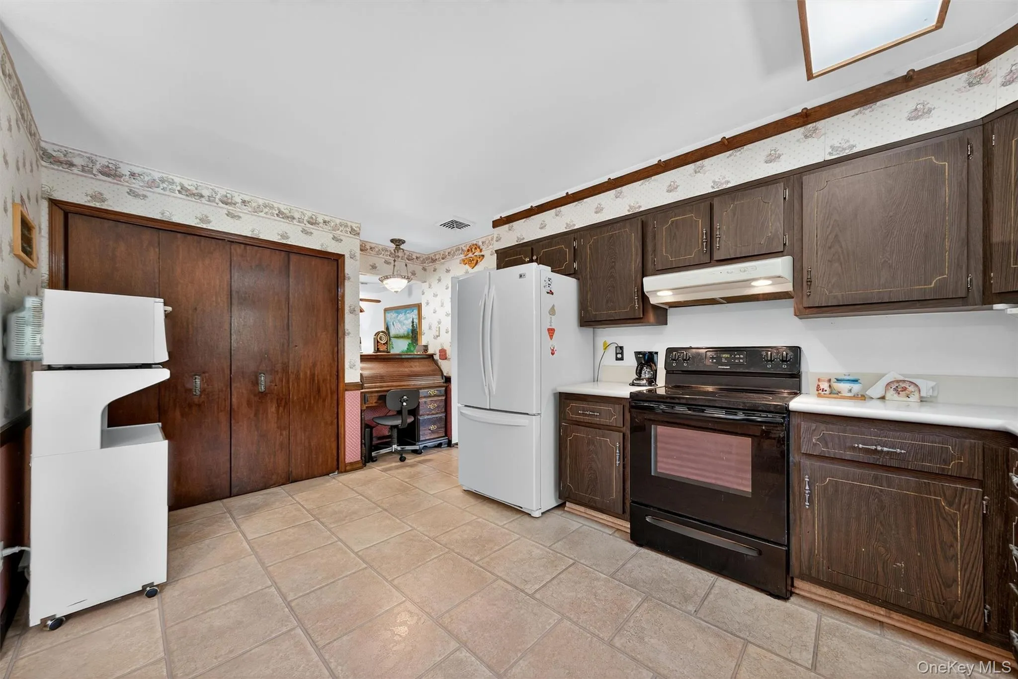 Kitchen featuring wallpapered walls, electric range, under cabinet range hood, freestanding refrigerator, and dark brown cabinets Kitchen featuring wallpapered walls, electric range, under cabinet range hood, freestanding refrigerator, and dark brown cabinets