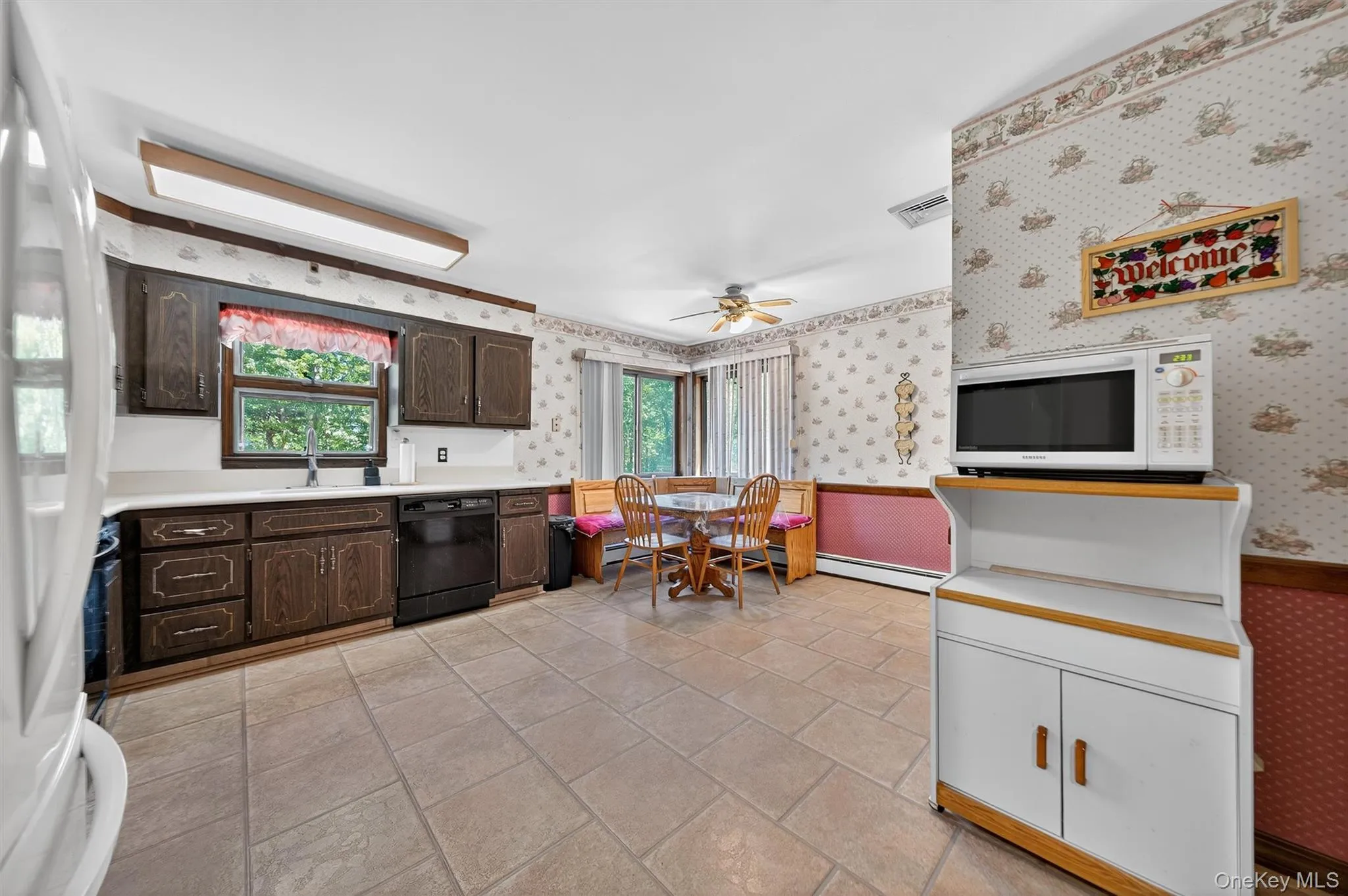 Kitchen with white appliances, wallpapered walls, dark brown cabinetry, light countertops, and a ceiling fan Kitchen with white appliances, wallpapered walls, dark brown cabinetry, light countertops, and a ceiling fan