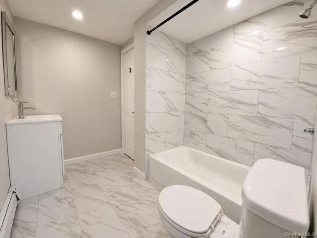 Spa-inspired primary bathroom featuring dual porcelain toilets, floating vanity with integrated sink, polished stone-finish flooring, and marble-look tile wall surround with linear layout Spa-inspired primary bathroom featuring dual porcelain toilets, floating vanity with integrated sink, polished stone-finish flooring, and marble-look tile wall surround with linear layout
