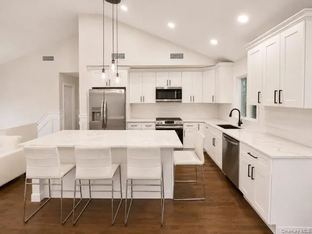 Modern kitchen featuring white shaker-style cabinetry, quartz countertops, stainless steel appliances including a gas range and built-in microwave, and a large center island with seating Modern kitchen featuring white shaker-style cabinetry, quartz countertops, stainless steel appliances including a gas range and built-in microwave, and a large center island with seating