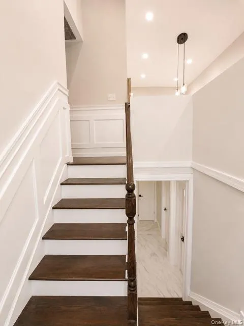 Elegant staircase featuring dark wood-finish treads with white risers, white wainscoting throughout, and a traditional turned wood balustrade Elegant staircase featuring dark wood-finish treads with white risers, white wainscoting throughout, and a traditional turned wood balustrade