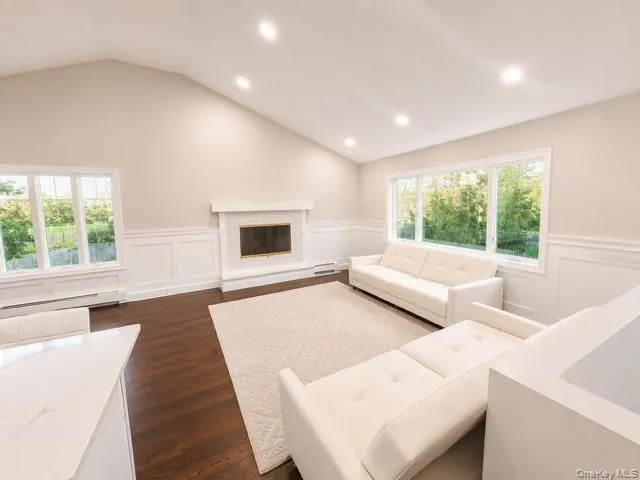 Spacious great room featuring vaulted ceilings with recessed lighting, large multi-pane windows flooding the space with natural light, a fireplace with surround, and warm wood-finish flooring throughout Spacious great room featuring vaulted ceilings with recessed lighting, large multi-pane windows flooding the space with natural light, a fireplace with surround, and warm wood-finish flooring throughout