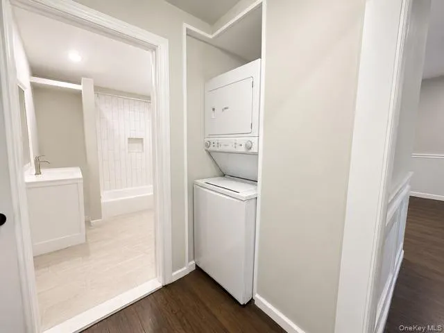 Full-size stackable washer and dryer, wood-finish flooring, and a bathroom featuring a white vanity with a brushed nickel faucet, a subway tile shower surround, and light-toned tile flooring Full-size stackable washer and dryer, wood-finish flooring, and a bathroom featuring a white vanity with a brushed nickel faucet, a subway tile shower surround, and light-toned tile flooring