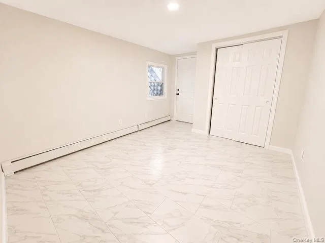 Light-colored walls, recessed ceiling lighting, baseboard heating, a panel door, and white tiled flooring Light-colored walls, recessed ceiling lighting, baseboard heating, a panel door, and white tiled flooring